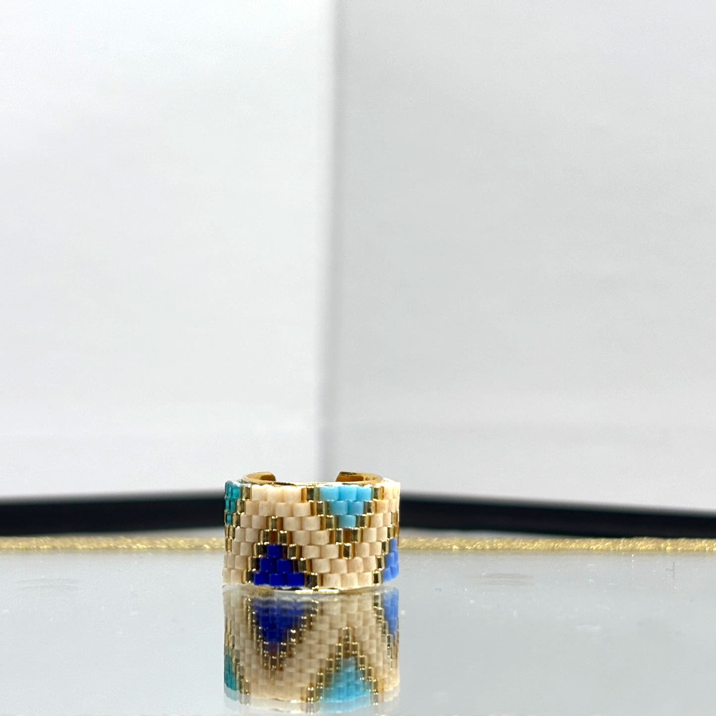 A beige triangle ear cuff featuring a geometric pattern, displayed on a reflective surface.