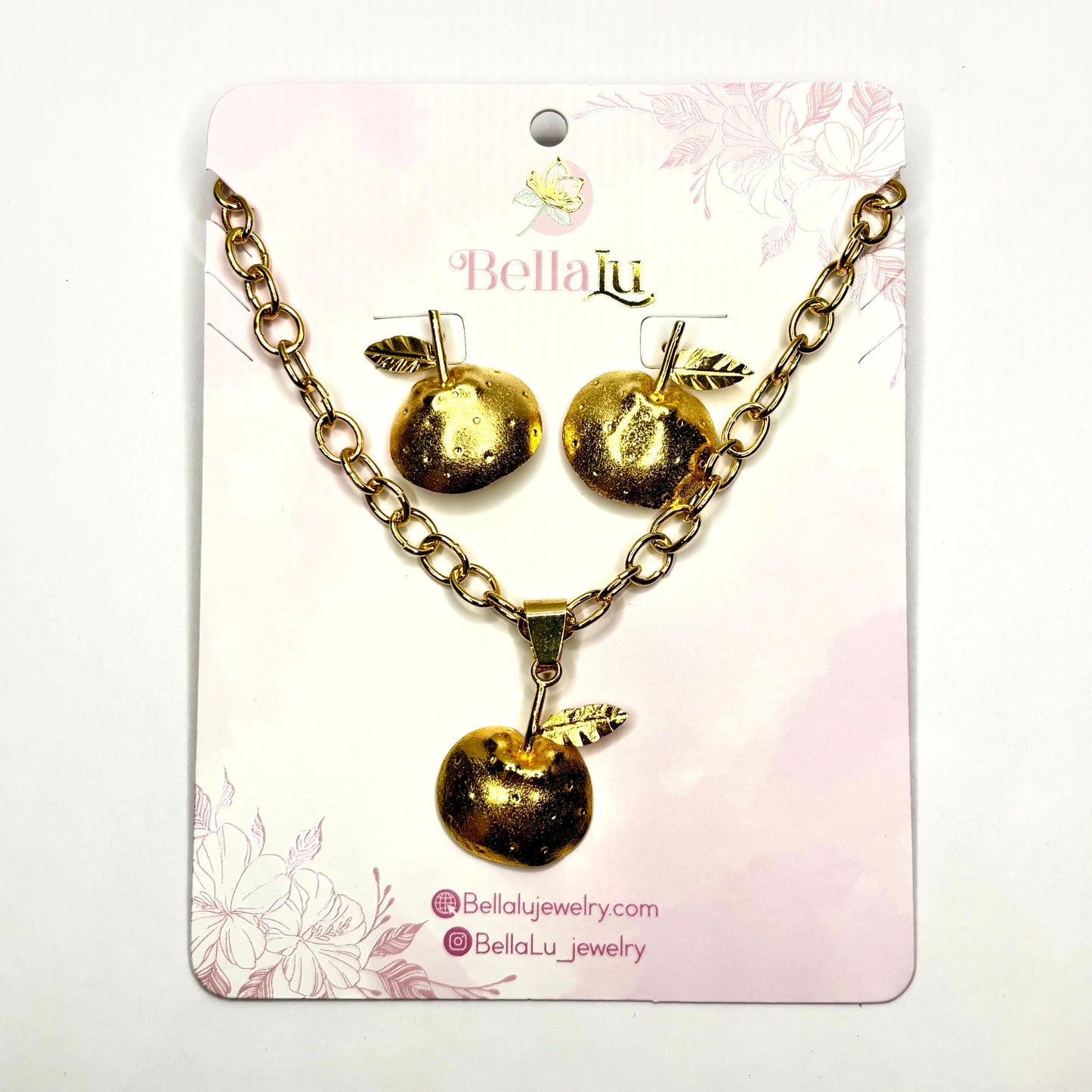 Gold apple necklace pear and earrings set on a Bella Lu branded card with floral designs.