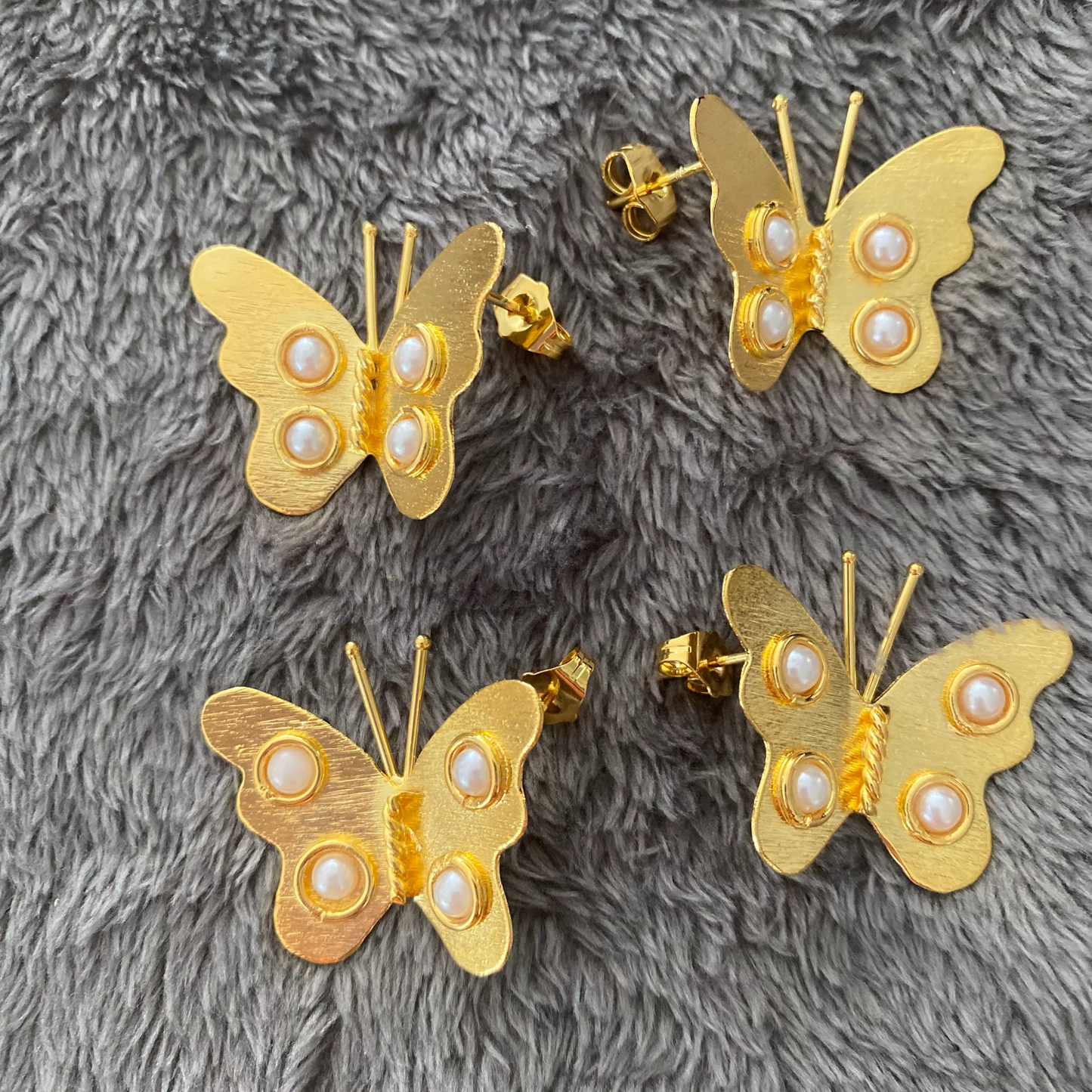 Gold butterfly earrings with pearl centers on a gray textured surface
