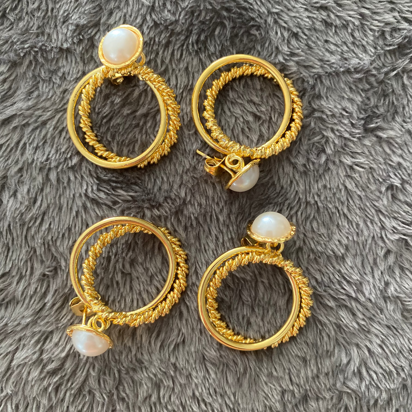 Gold hoop earrings with pearl-like stones on a gray fluffy surface