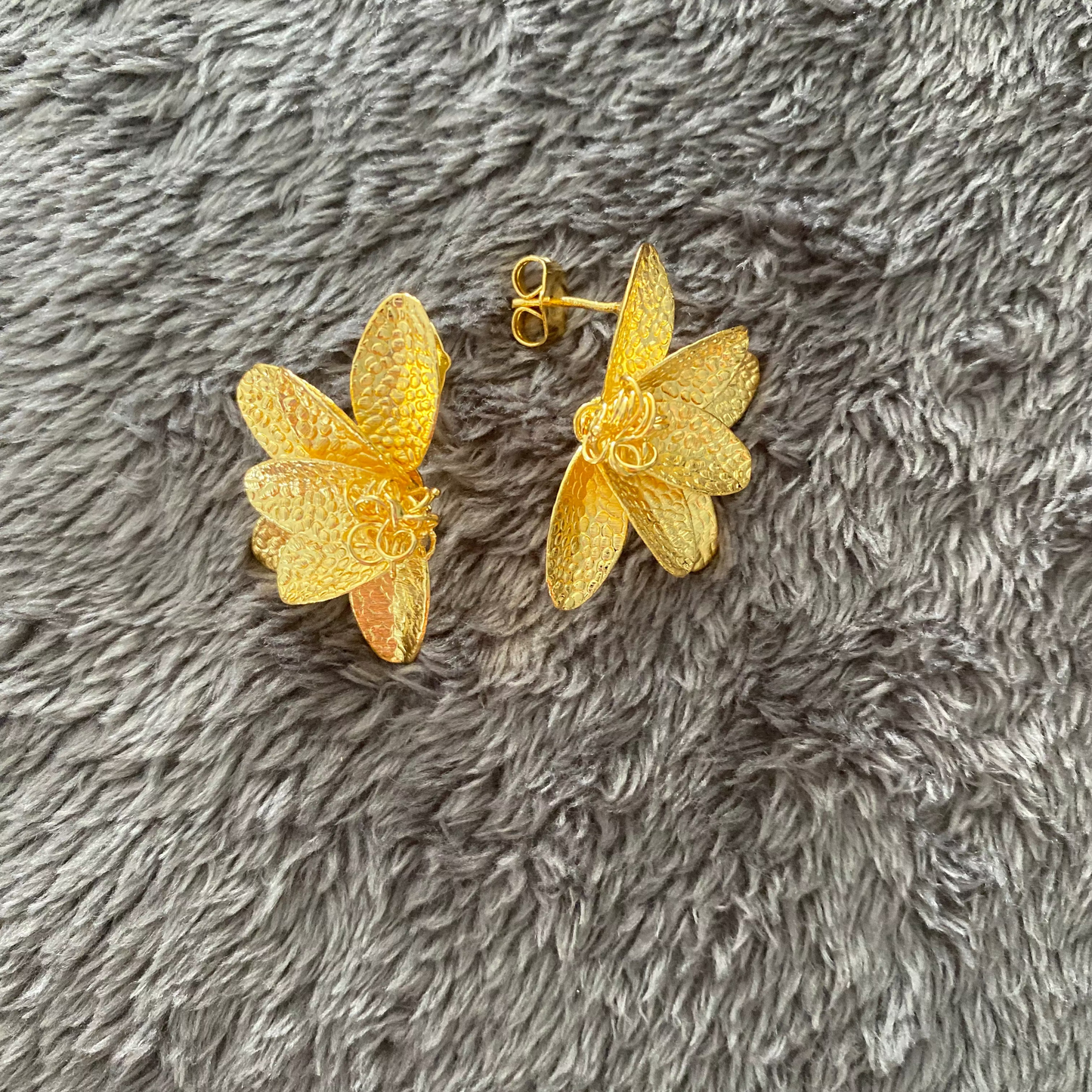 Gold half flower earrings on a gray textured surface