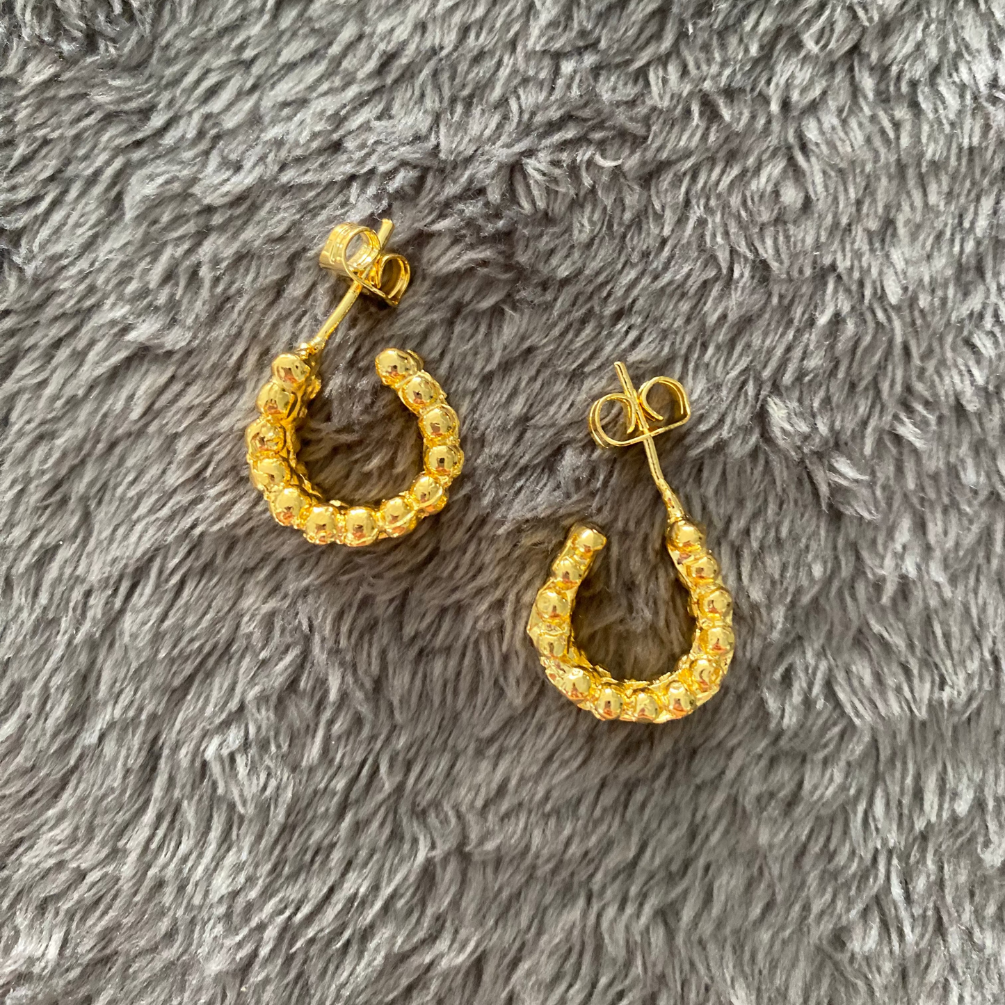 Gold hoop earrings on a gray fluffy surface