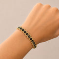 A gold beaded bracelet with black flower-shaped beads, shown worn on a person's wrist against a plain beige background.