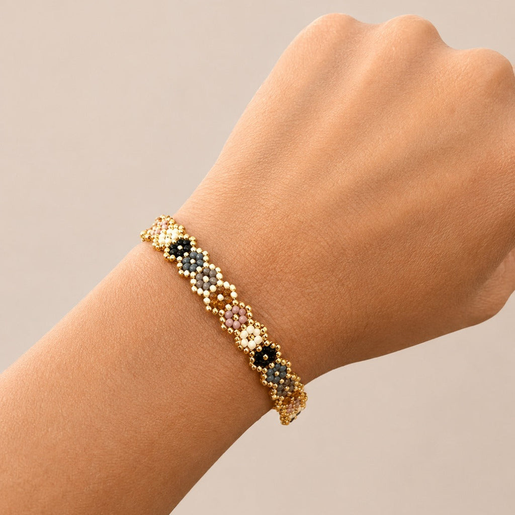 A gold-toned beaded bracelet with multicolored floral details, shown worn on a person's wrist against a plain beige background.