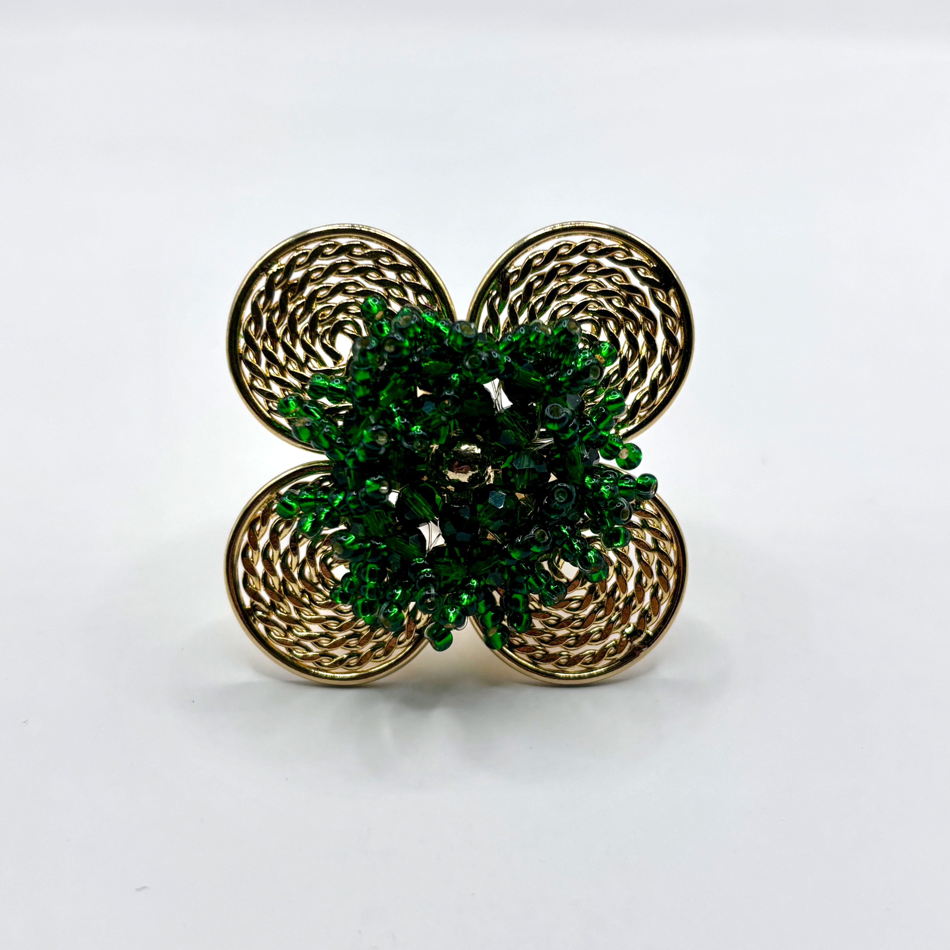 A handcrafted bronze ring with a gold plated design, featuring a flower shape with green beads and a textured pattern.