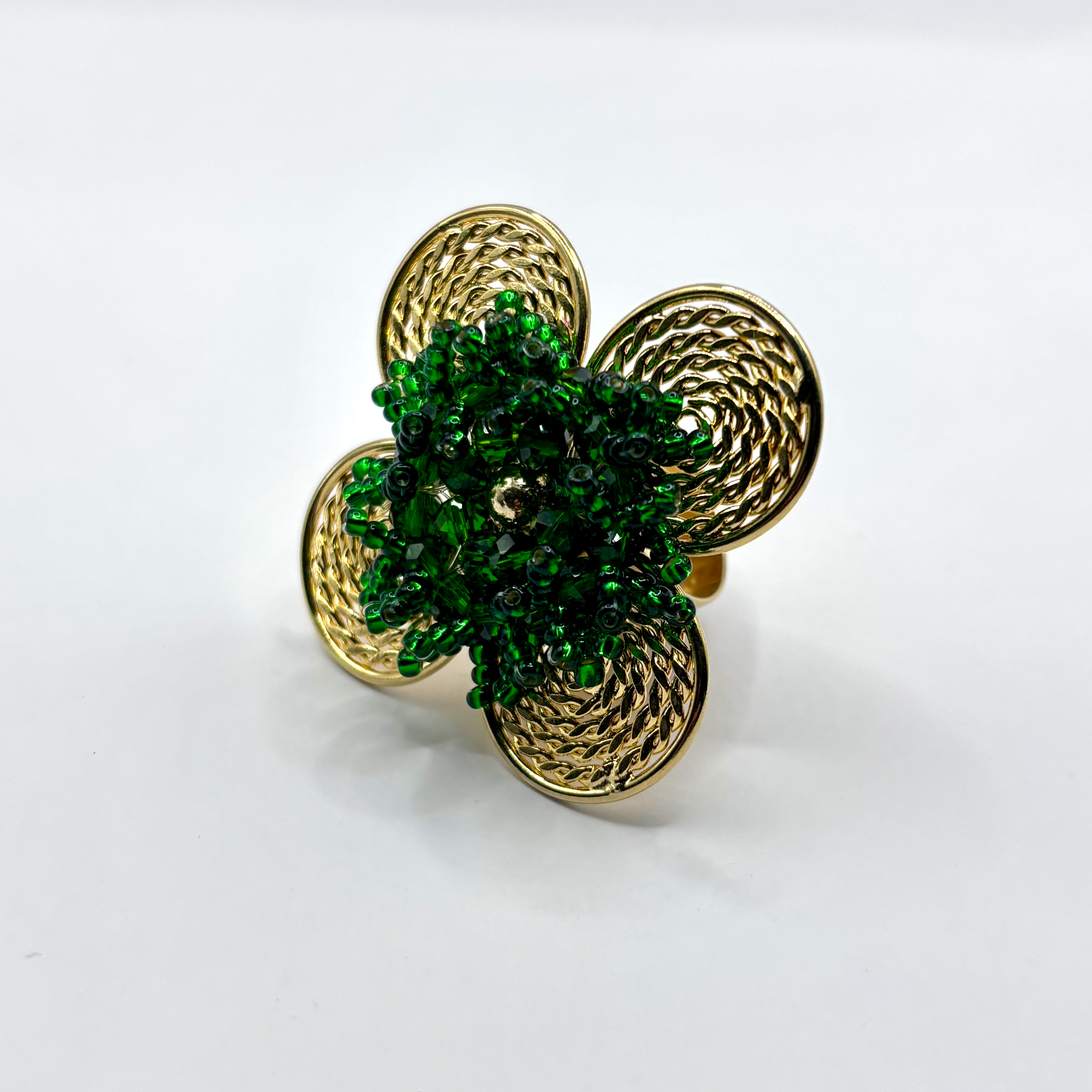 A handcrafted bronze ring with a gold plated design, featuring a flower shape with green beads and a textured pattern.