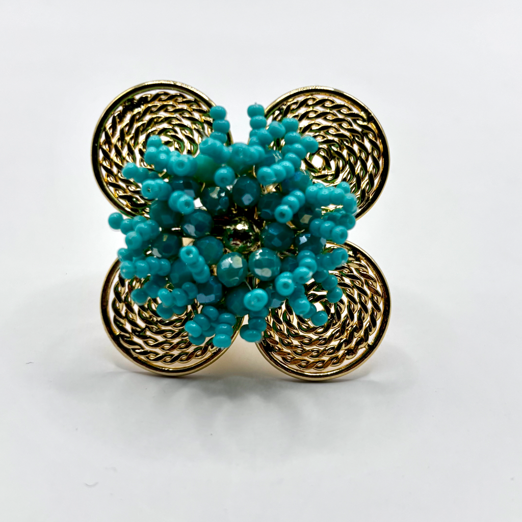 A handcrafted bronze ring with a gold plated design, featuring a flower shape with green beads and a textured pattern.