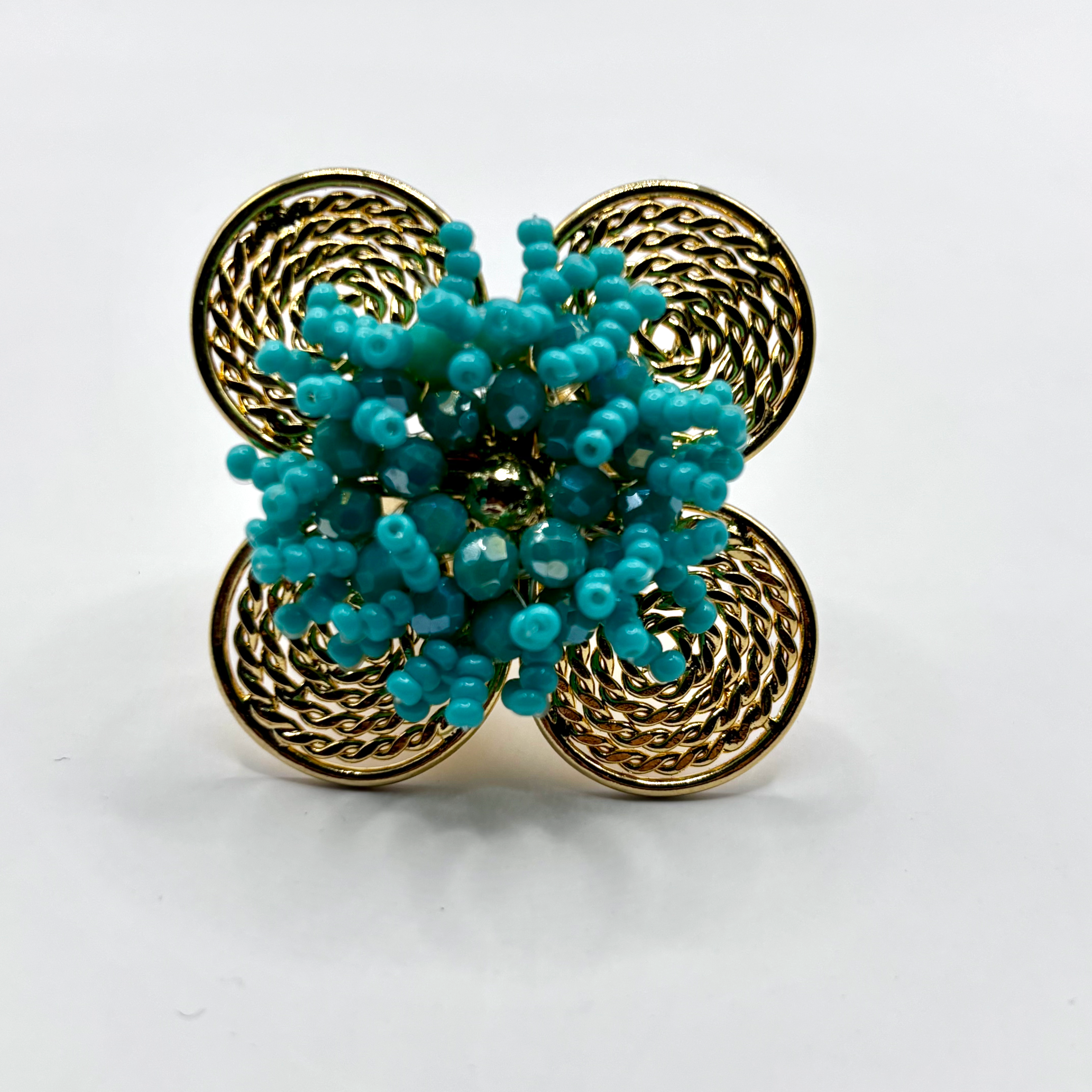 A handcrafted bronze ring with a gold plated design, featuring a flower shape with green beads and a textured pattern.