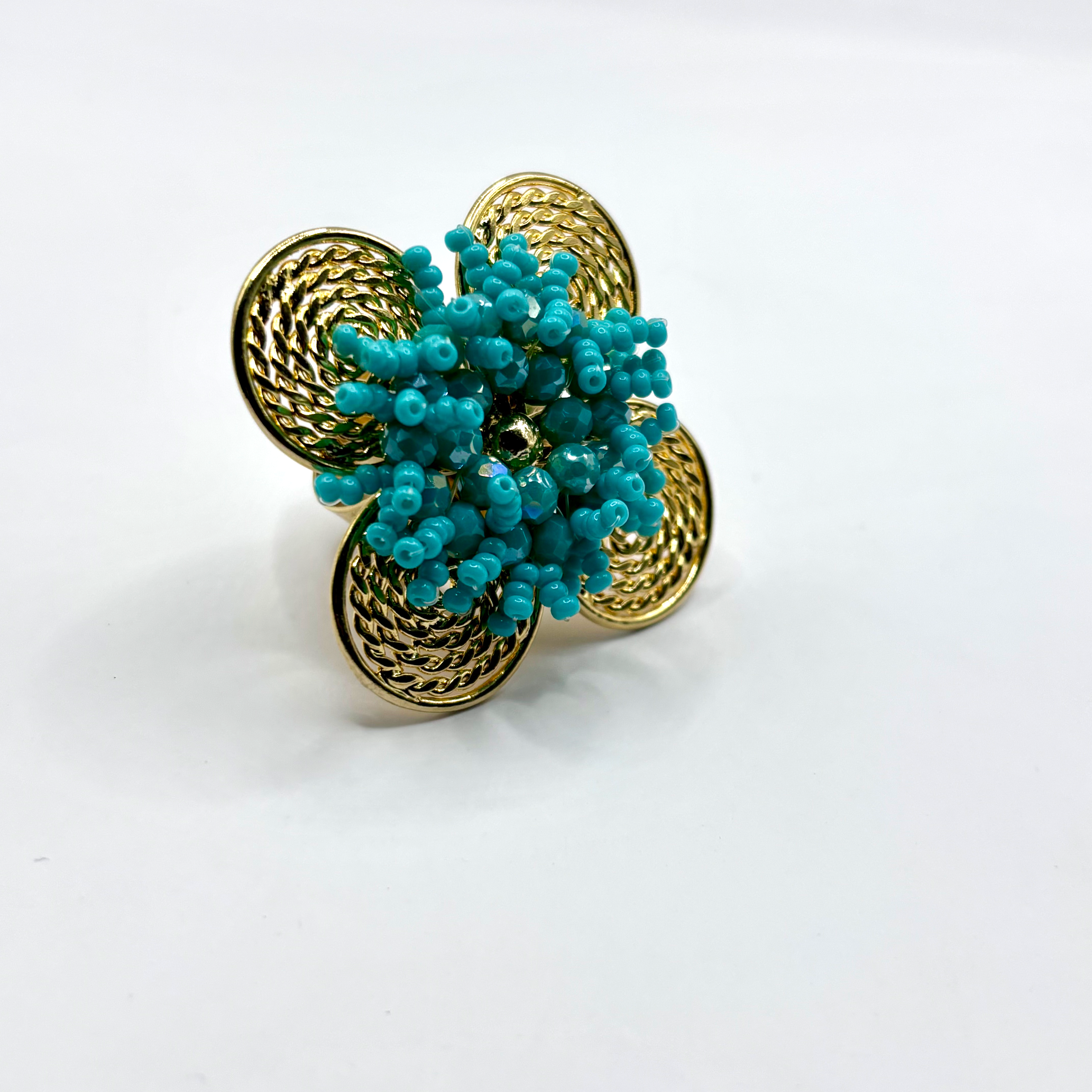A handcrafted bronze ring with a gold plated design, featuring a flower shape with green beads and a textured pattern.