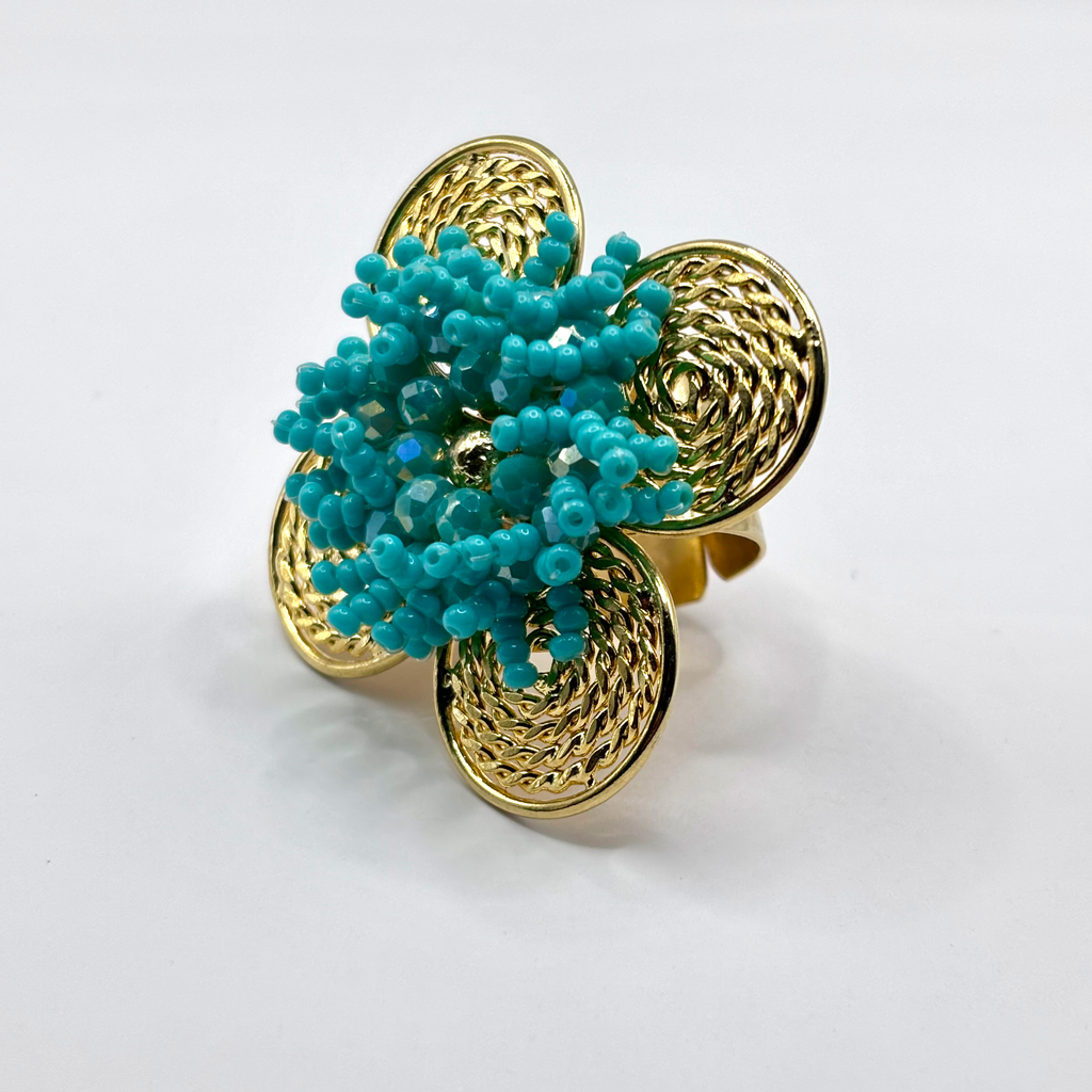 A handcrafted bronze ring with a gold plated design, featuring a flower shape with green beads and a textured pattern.