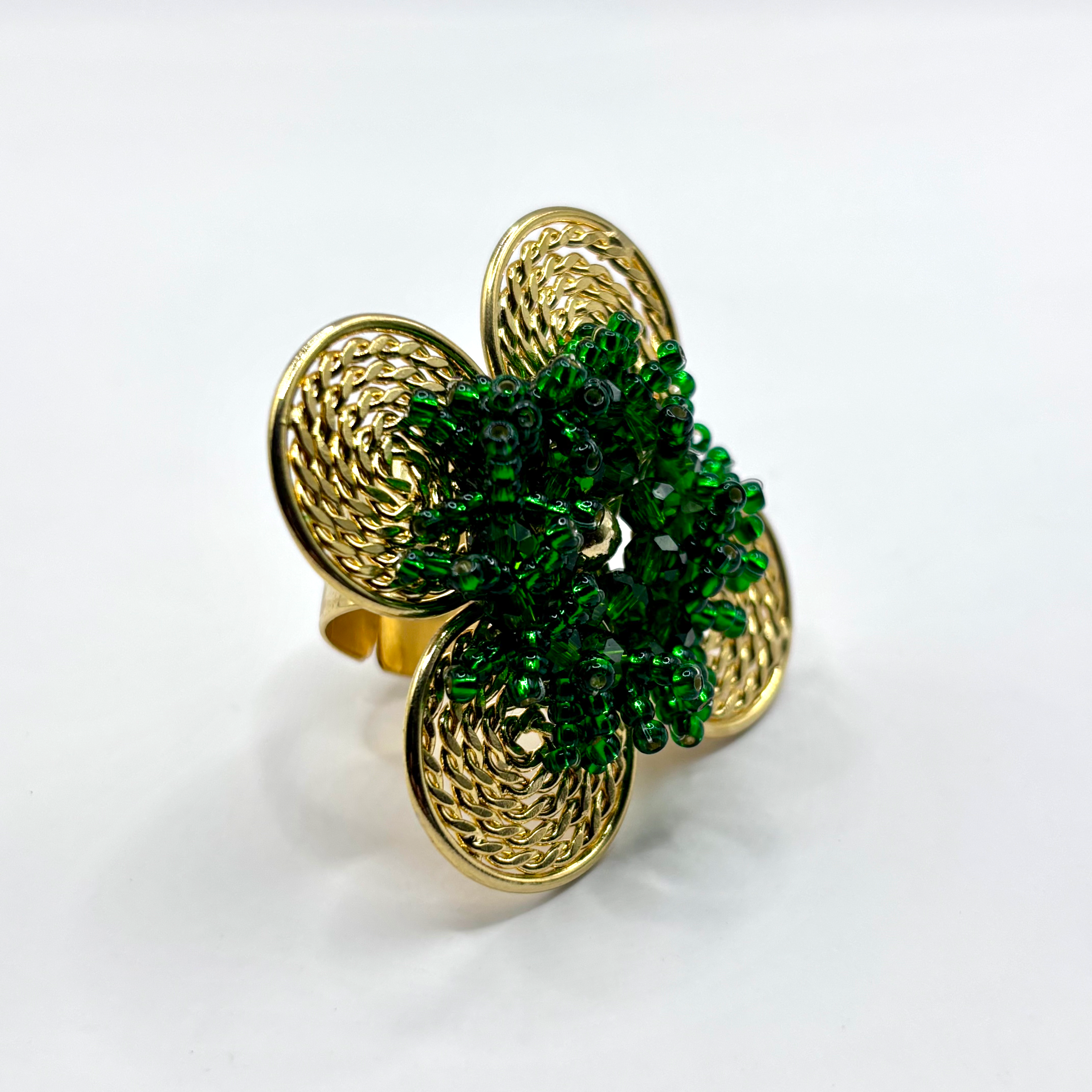 A handcrafted bronze ring with a gold plated design, featuring a flower shape with green beads and a textured pattern.
