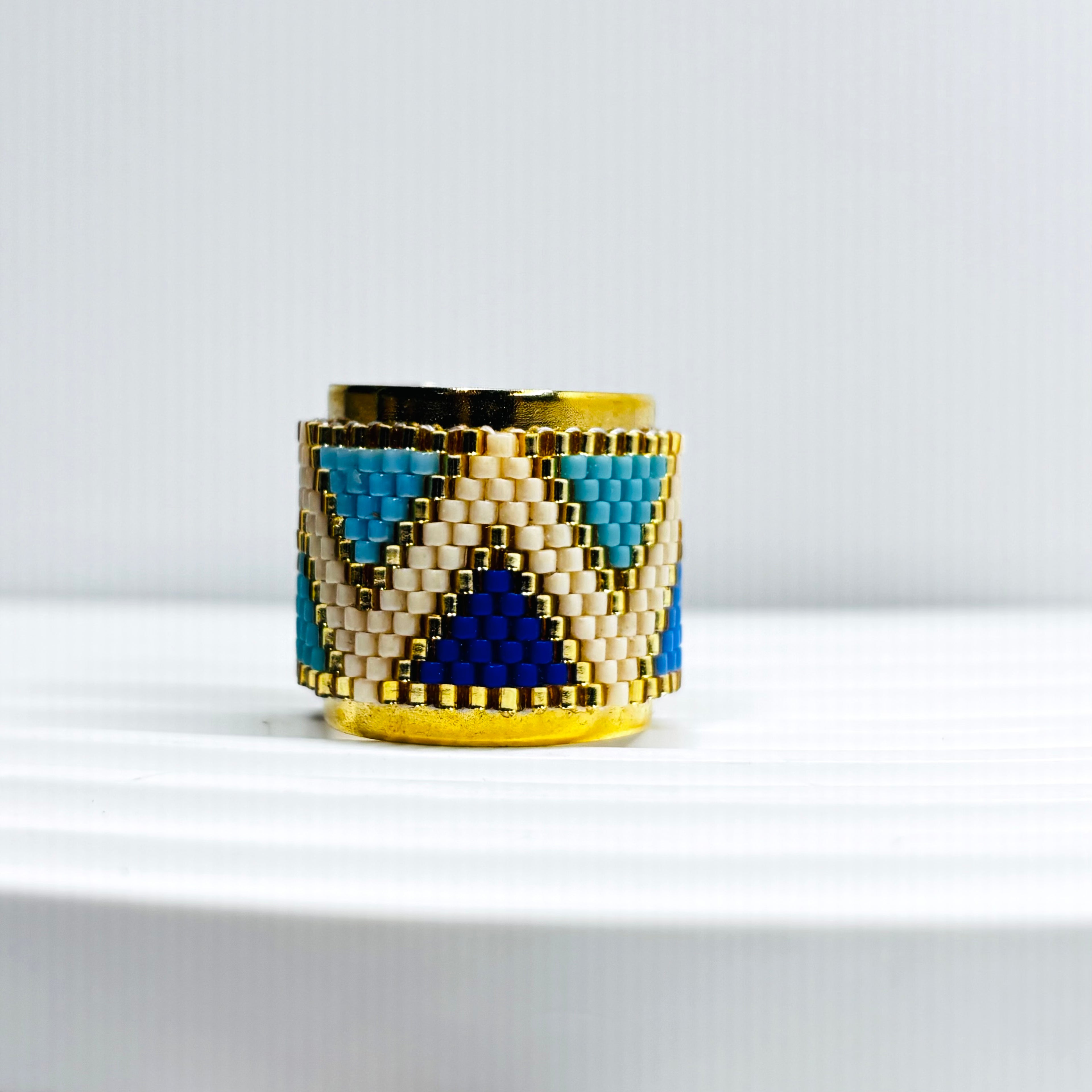 A handcrafted Miyuki bead ring with a geometric pattern, featuring small triangle details in blue and gold colors.