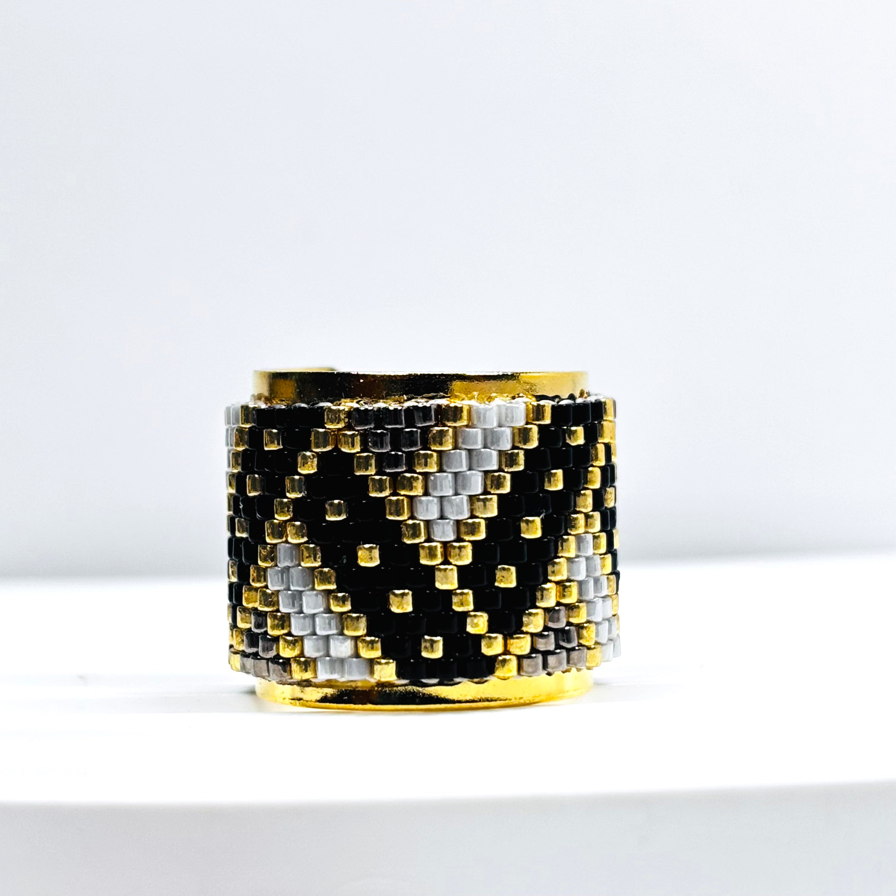 A handcrafted ring with black and gold Miyuki beads, featuring a geometric pattern and a 24k plated design.