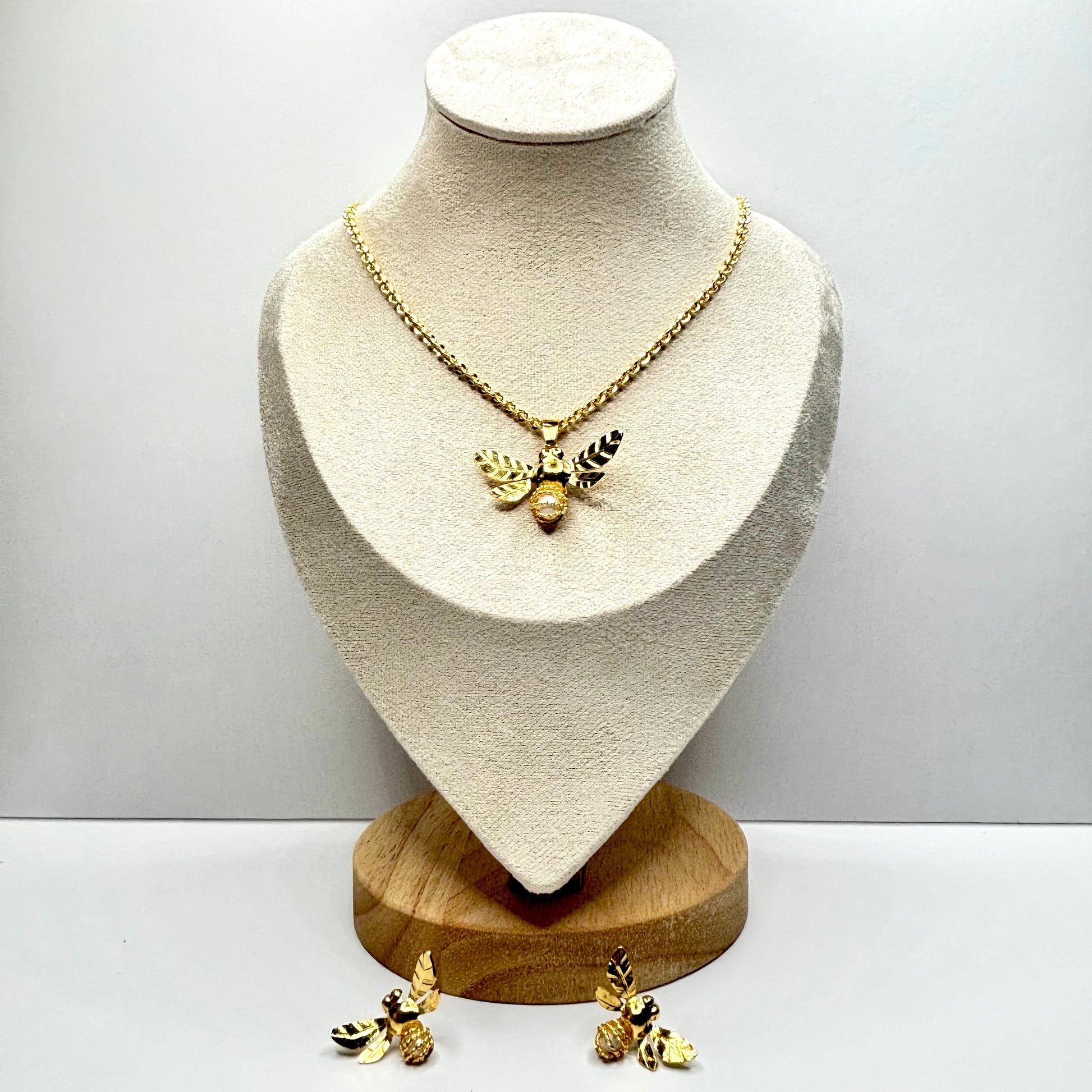 Gold necklace  bee and earrings on a mannequin bust with a plain background