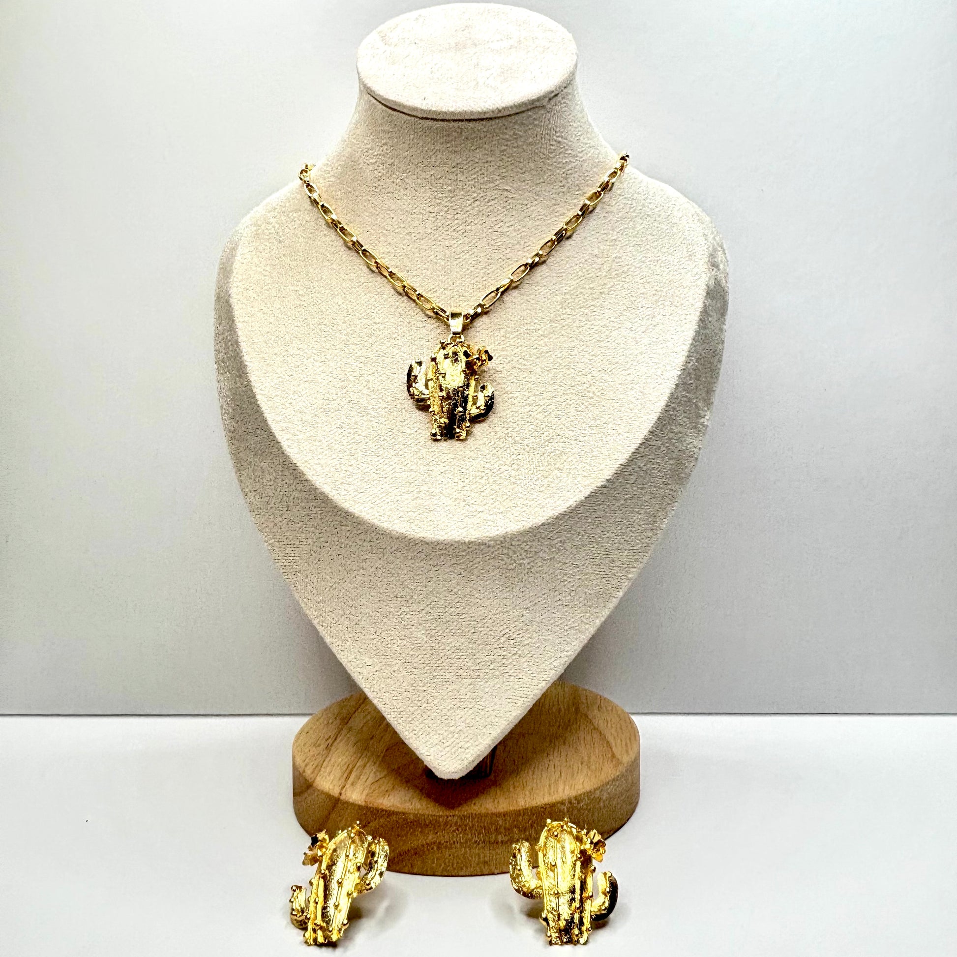 Gold necklace cactus and earrings on a mannequin bust with a plain background