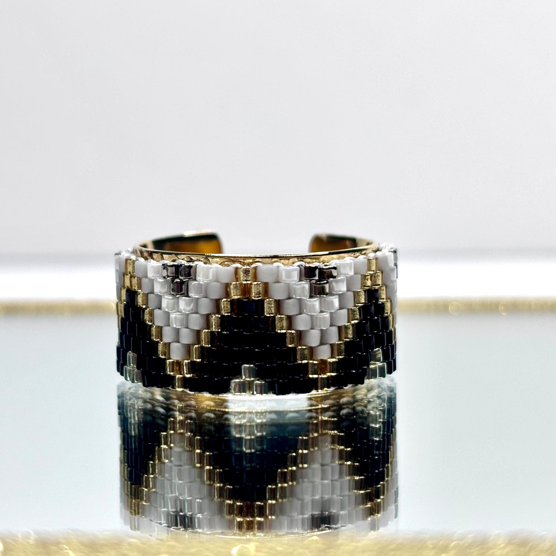 Cuff bracelet with black, white, and gold pattern on a light gray background