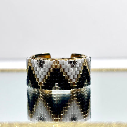 Cuff bracelet with black, white, and gold pattern on a light gray background