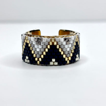 Beaded cuff bracelet with black, white, and gold pattern on a white background