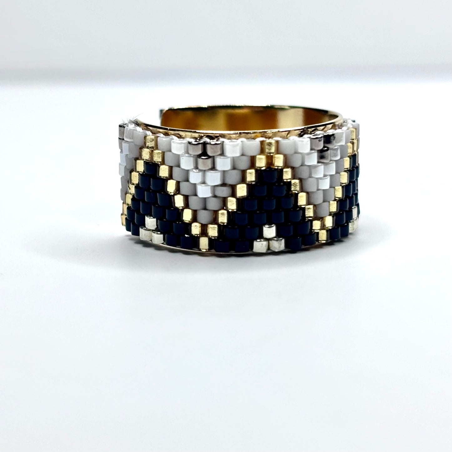 Beaded cuff bracelet with gold, black, and white pattern on a white background