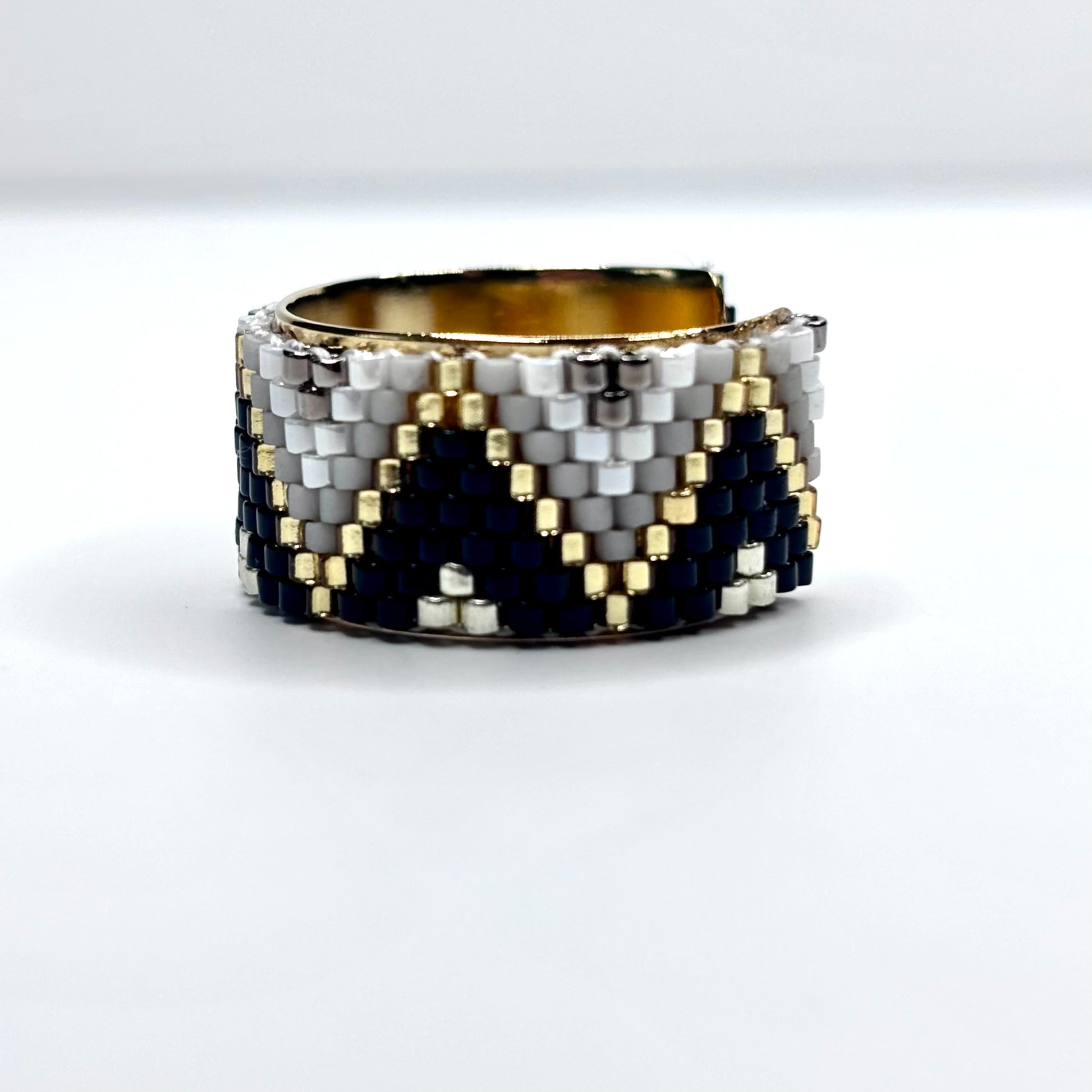 Beaded ring with black, white, and gold pattern on a white background