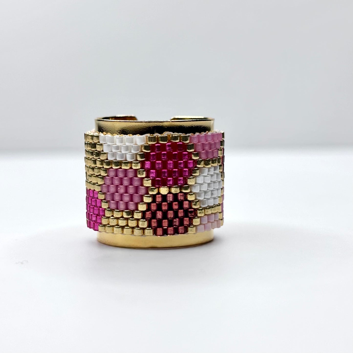 Beaded ring with pink, white, and gold pattern on a white background