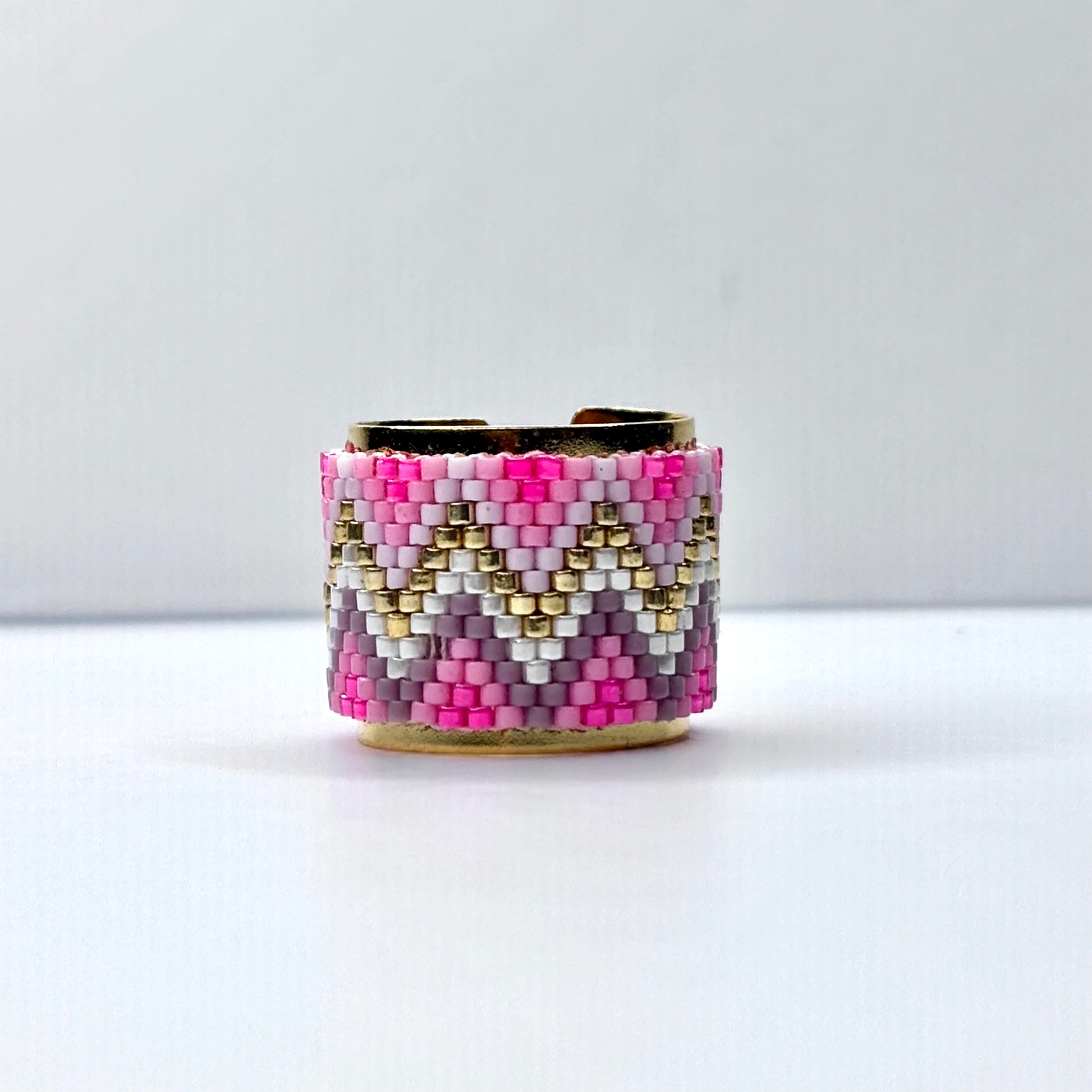 Beaded cuff bracelet with pink, gold, and white pattern on a white background
