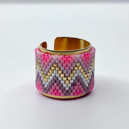 Beaded ring with pink, gold, and gray pattern on a reflective surface