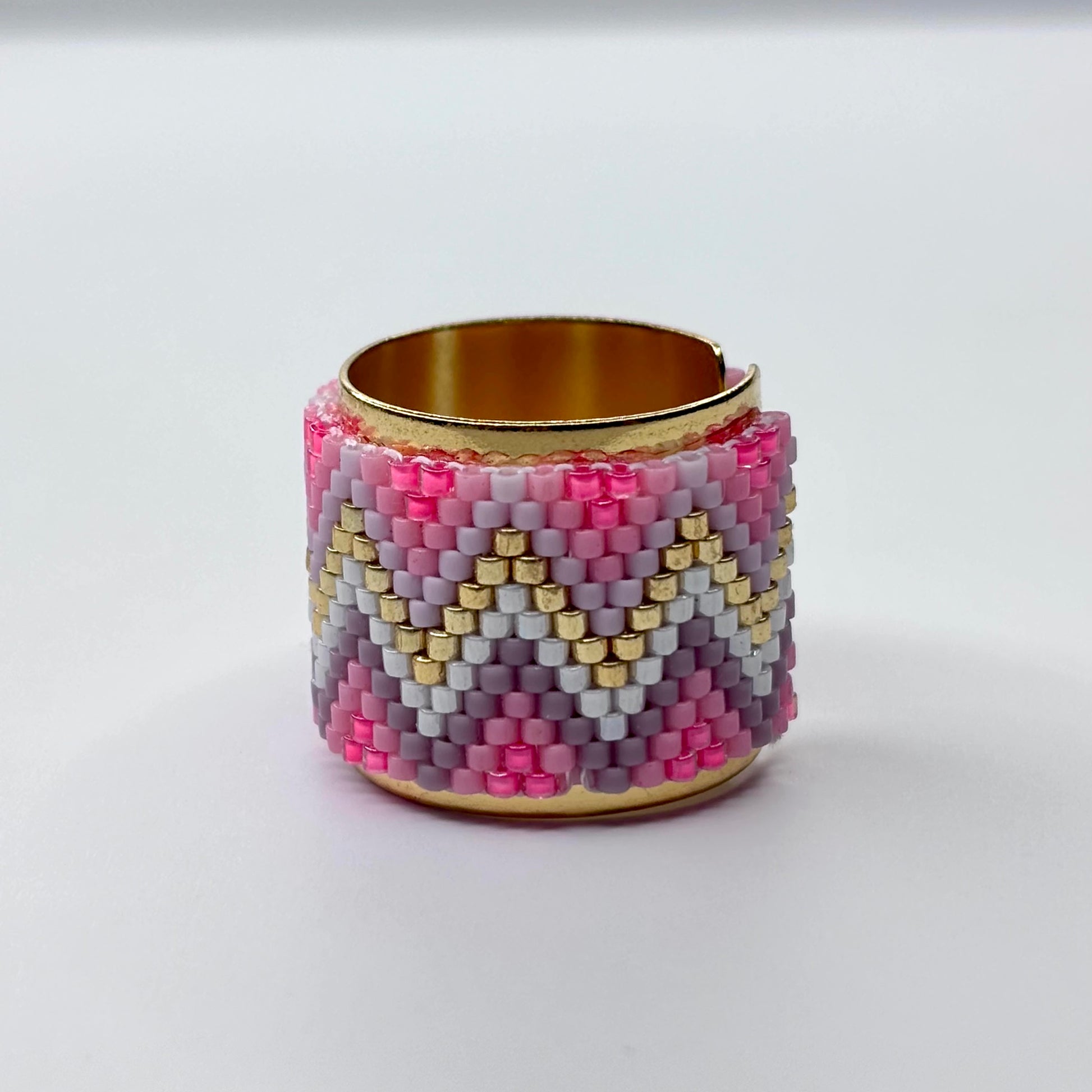 Beaded ring with pink, gold, and gray pattern on a reflective surface