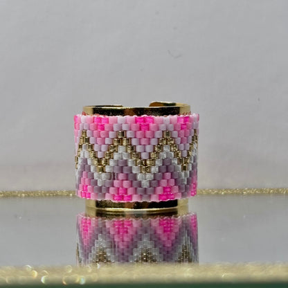 Beaded ring with pink, gold, and gray pattern on a reflective surface