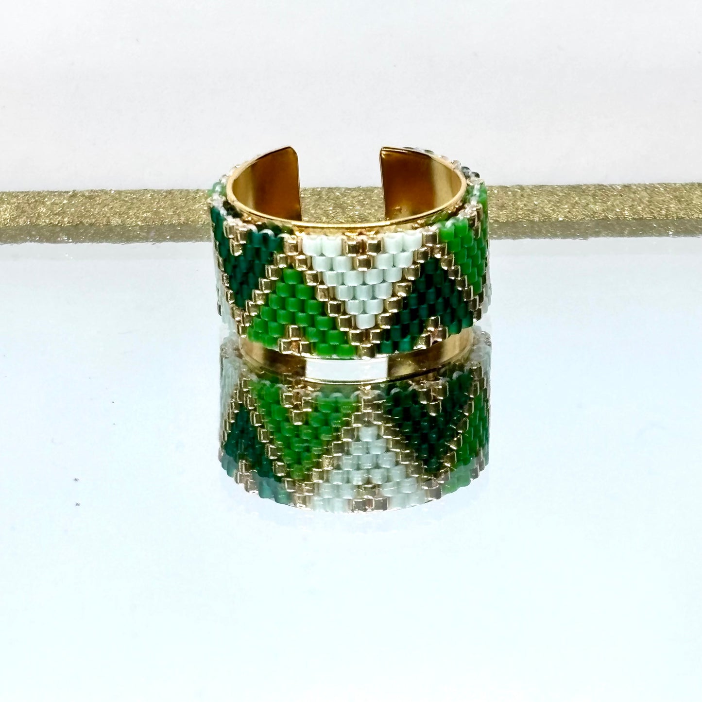 Beaded ring with green, gold, and white pattern on a white background
