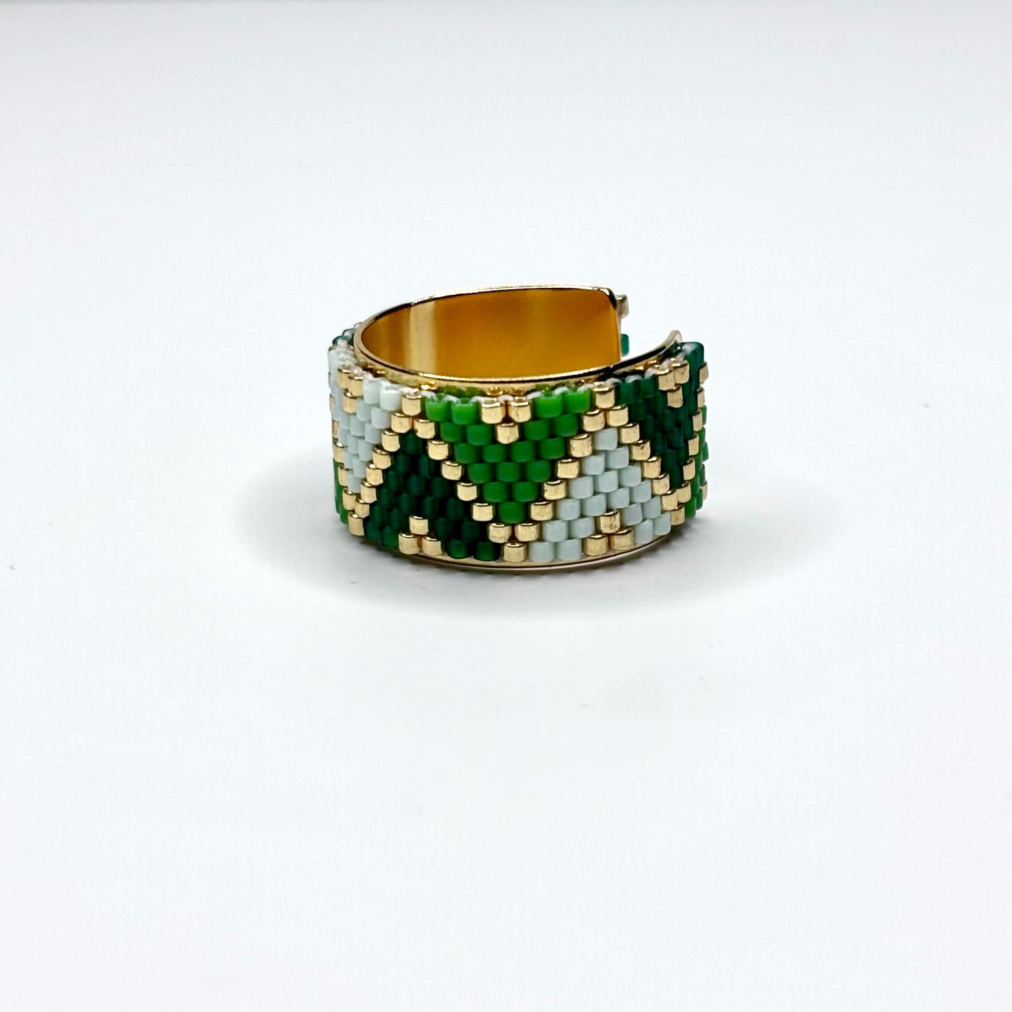 Beaded ring with green, gold, and white pattern on a white background