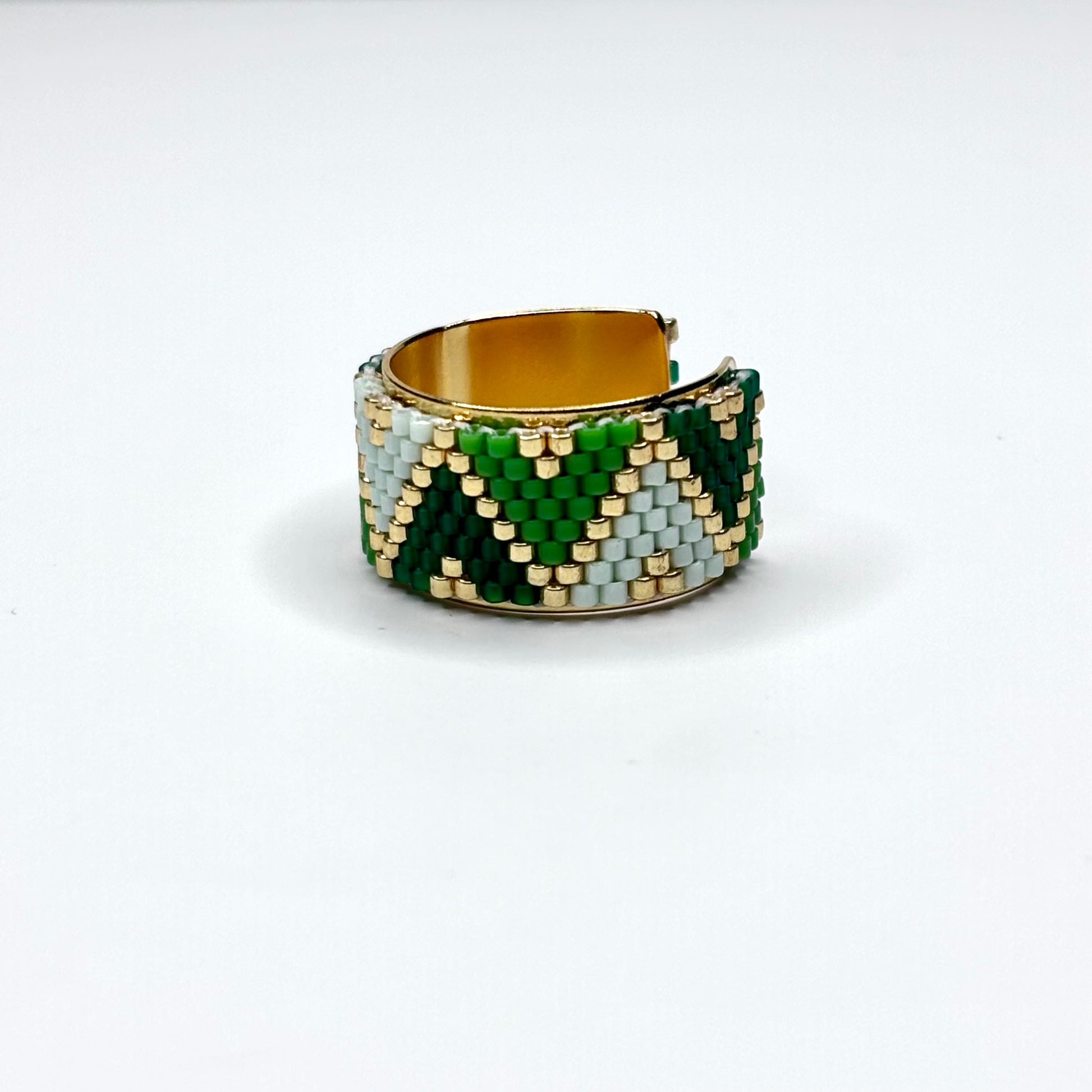 Beaded ring with green, gold, and white pattern on a white background