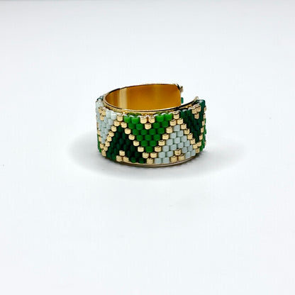 Beaded ring with green, gold, and white pattern on a white background