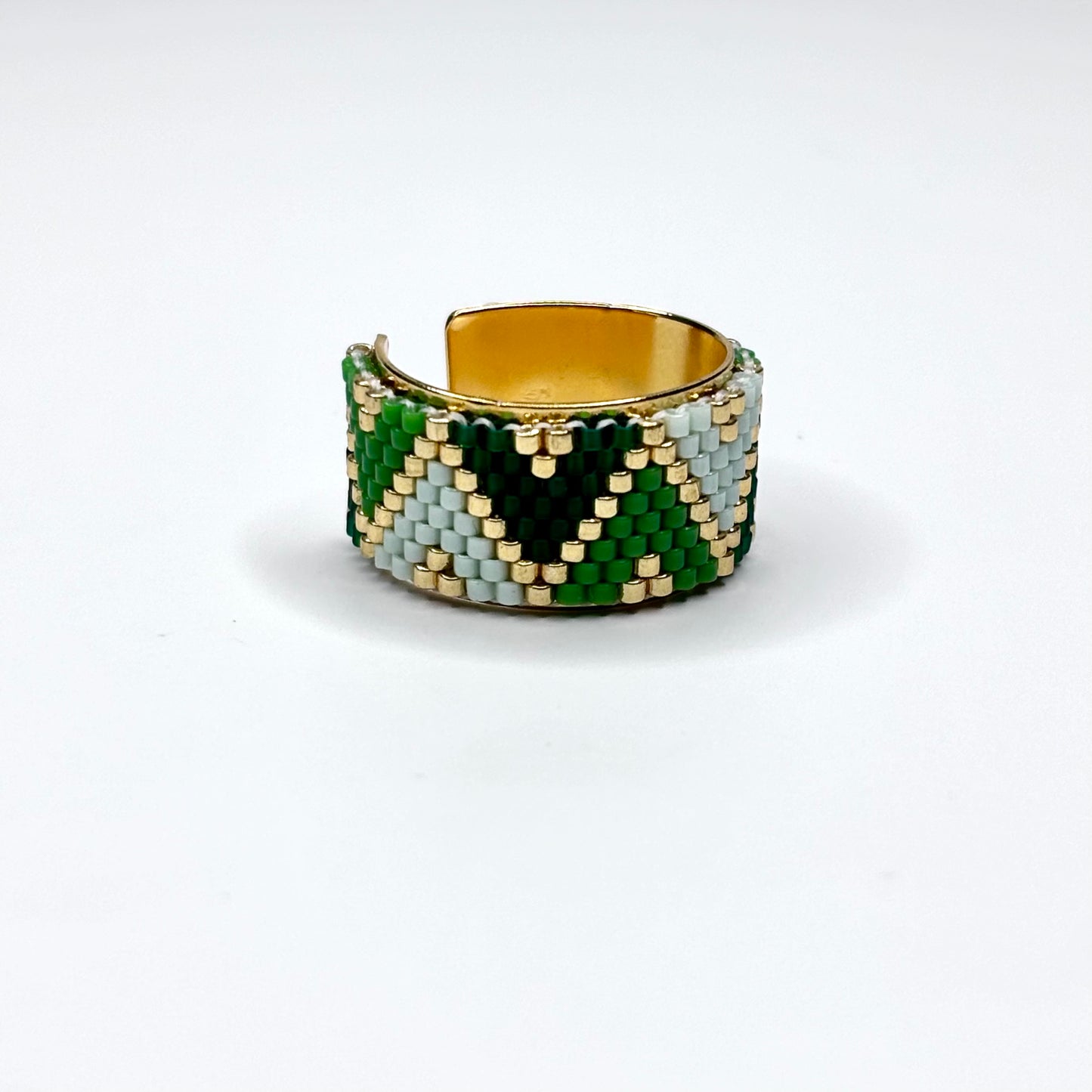 Beaded ring with green, gold, and white pattern on a white background