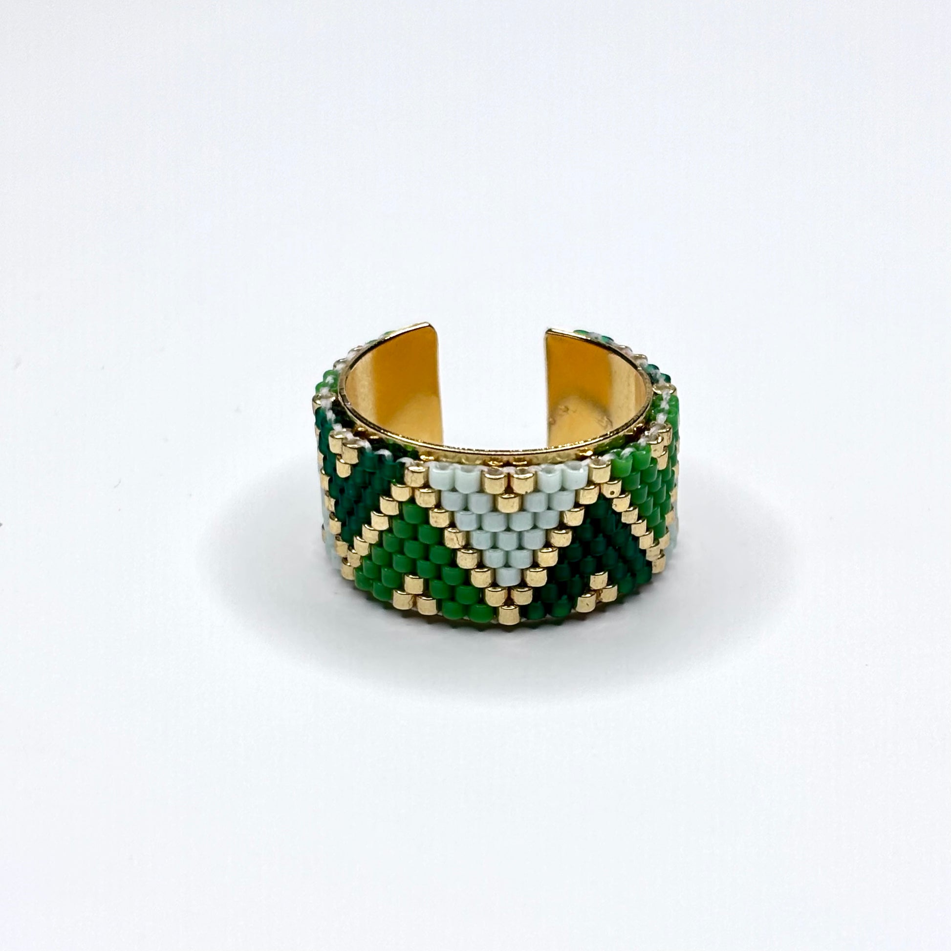Beaded ring with green, gold, and white pattern on a white background