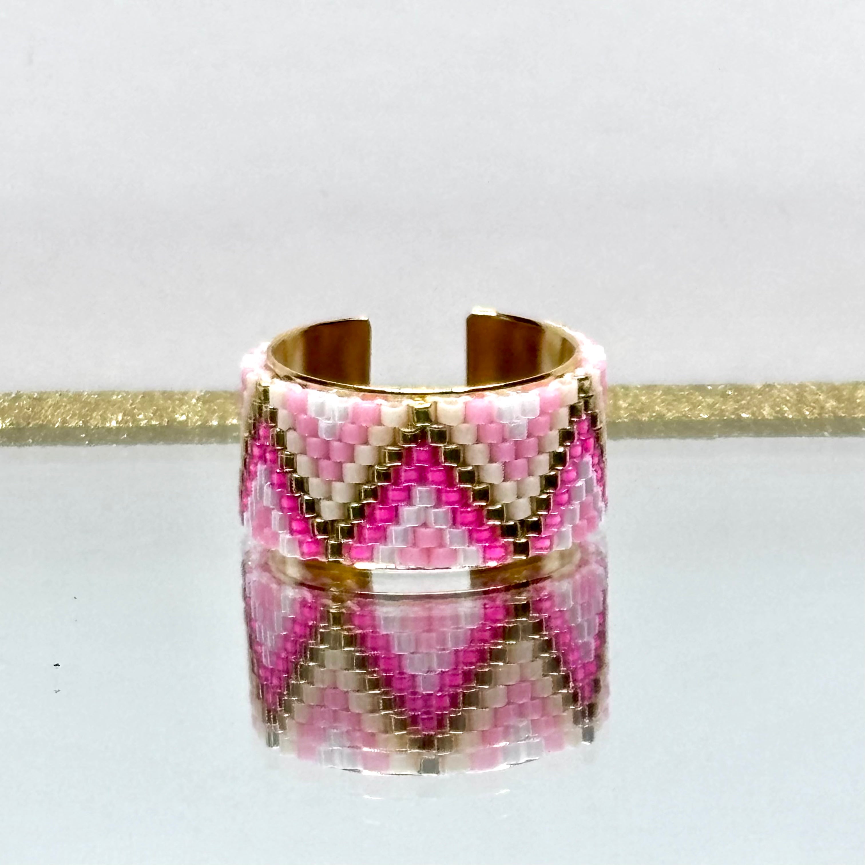 Beaded ring with pink, white, and gold pattern on a white background