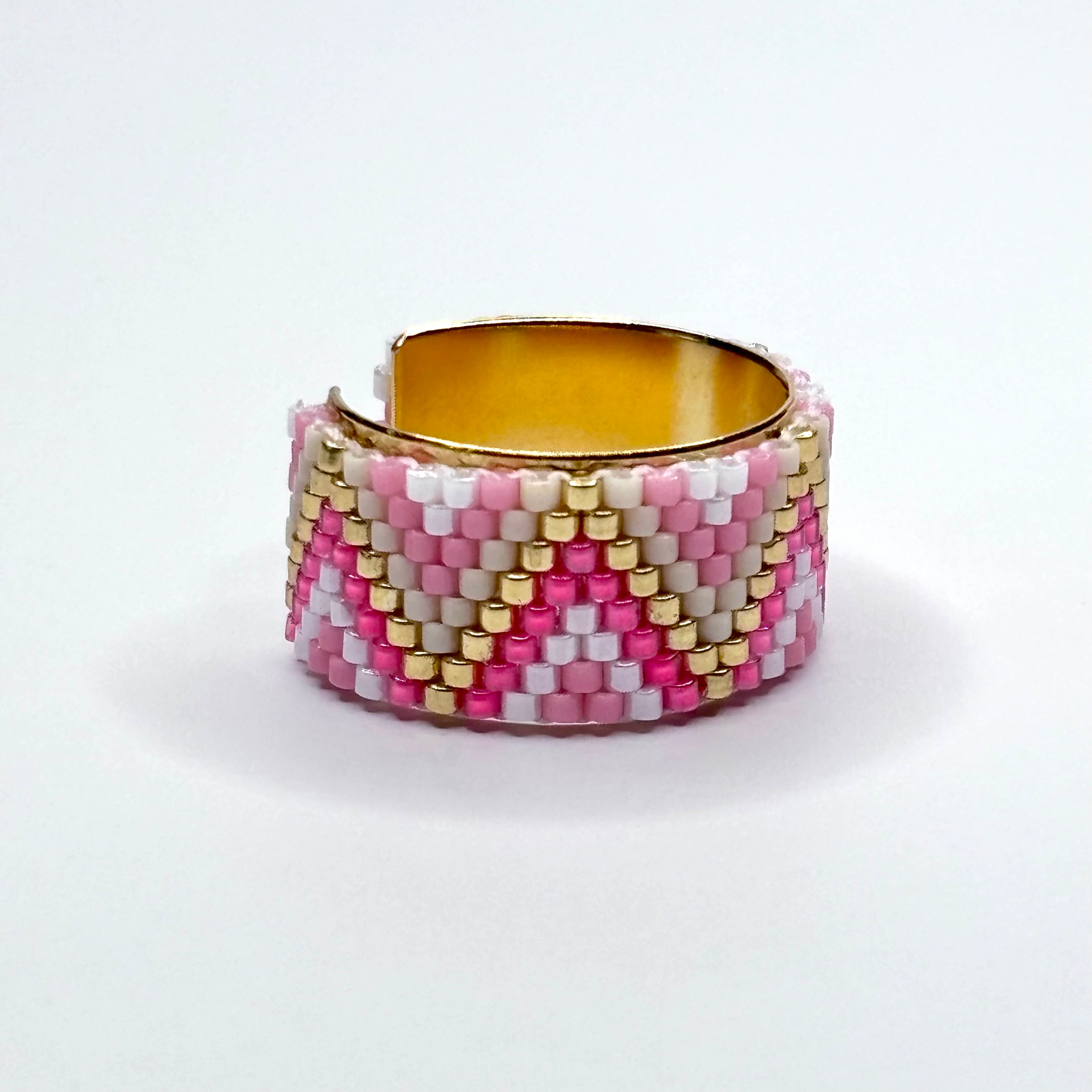 Beaded ring with pink, white, and gold pattern on a white background