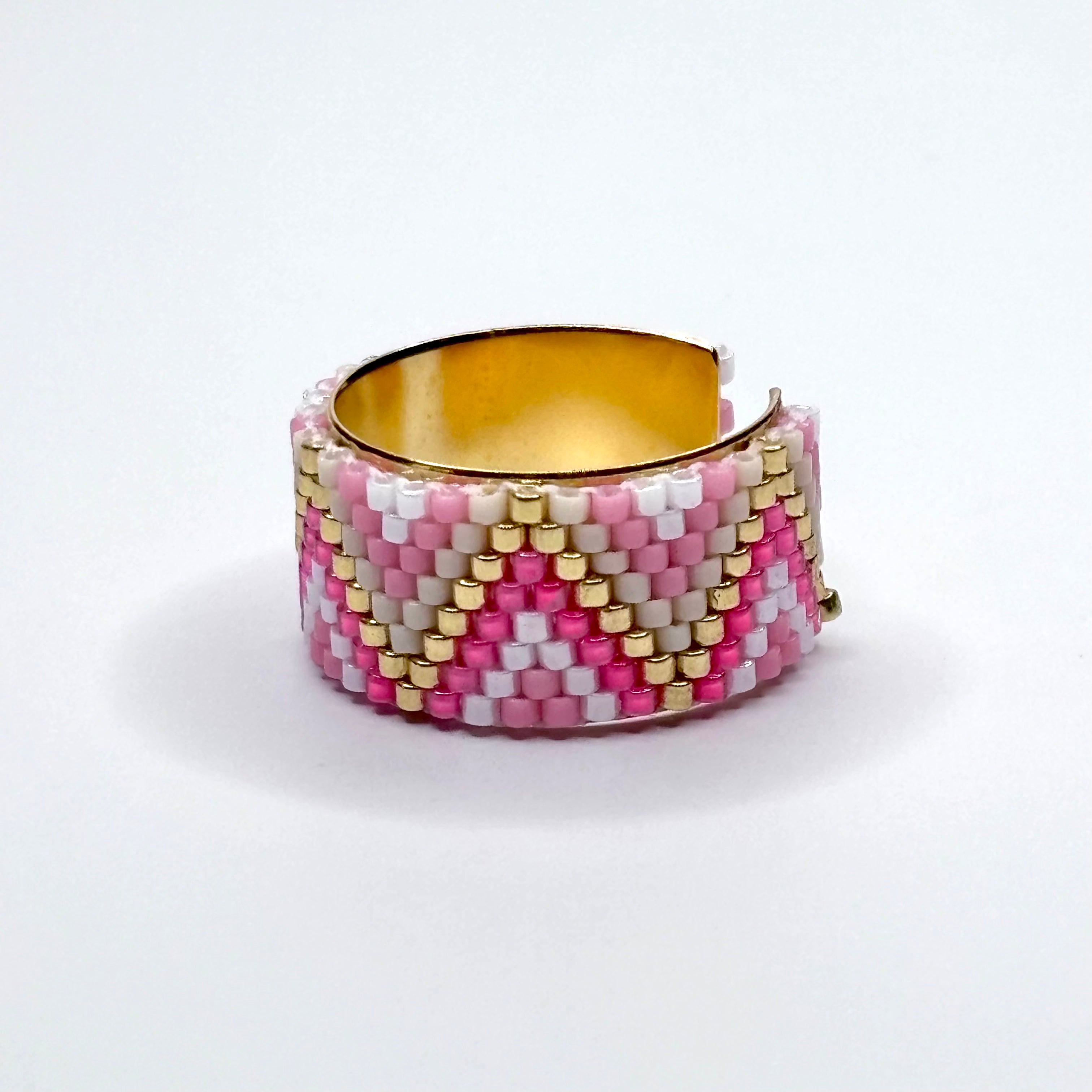 Beaded ring with pink, white, and gold pattern on a white background
