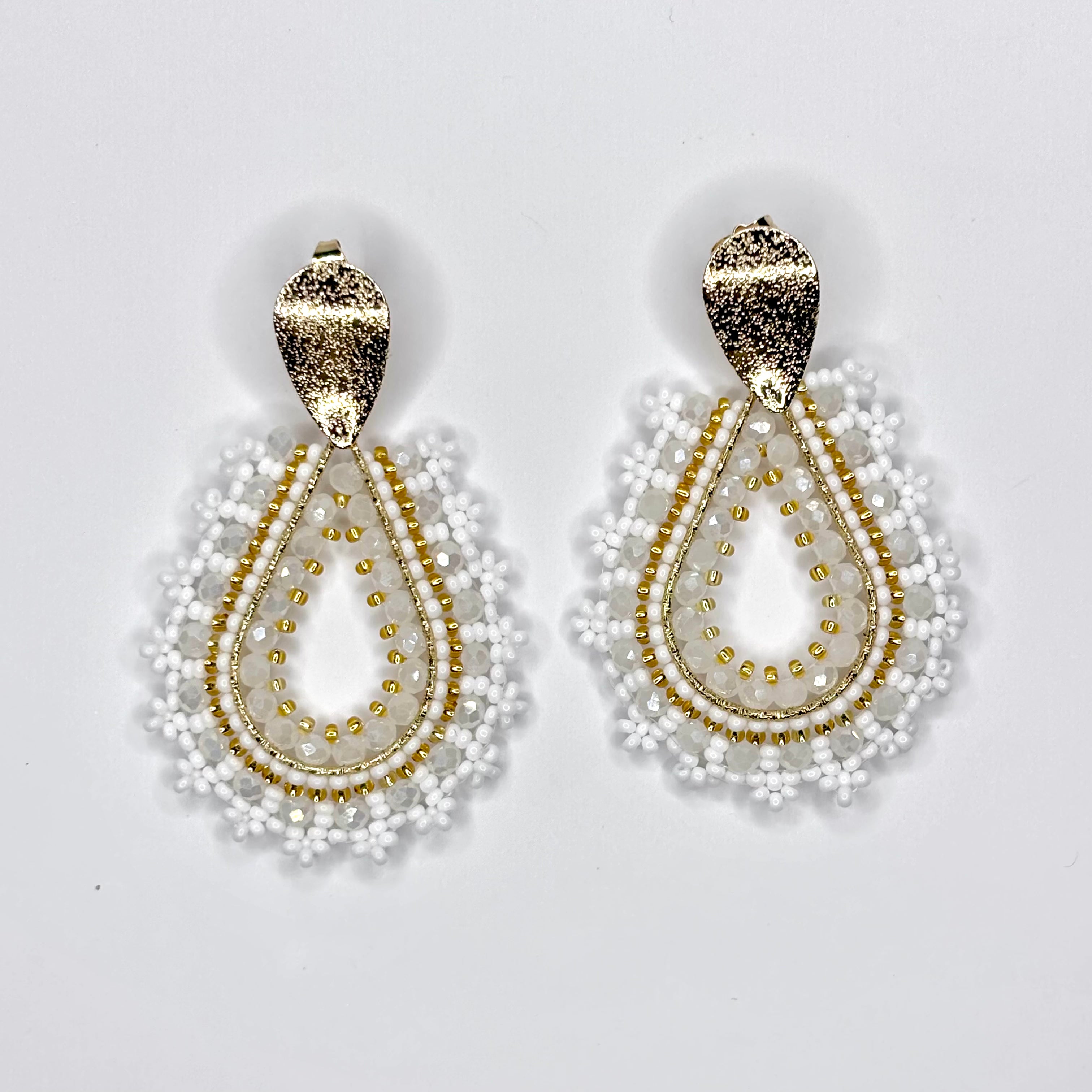 Pair of gold and white beaded earrings on a light gray background