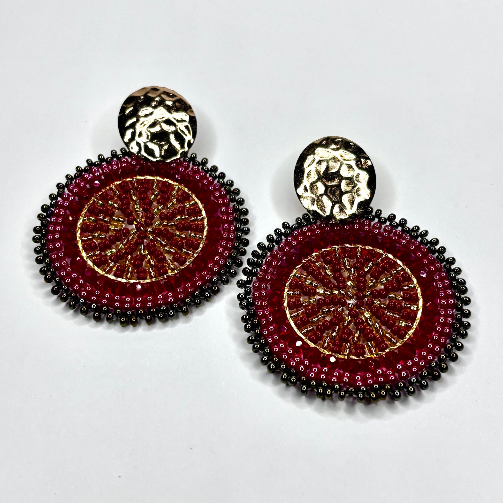 Pair of beaded earrings with gold and red design on a white background