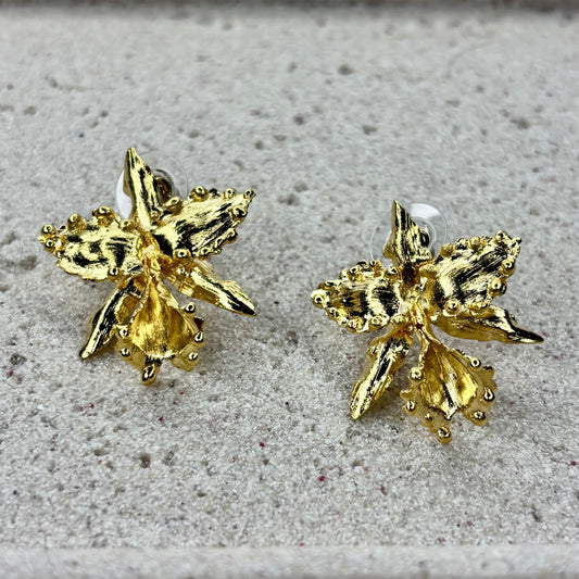 Pair of gold orchid-shaped earrings on a textured surface