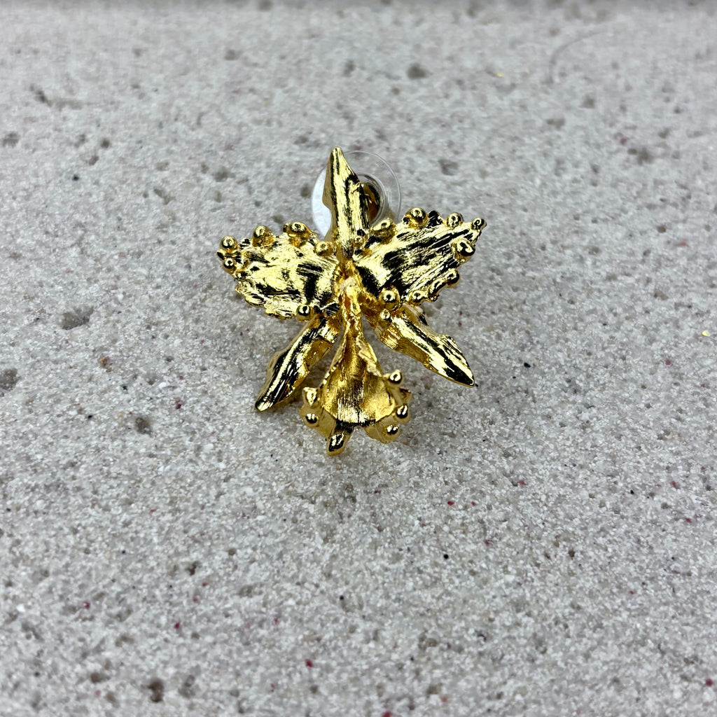 Pair of gold orchid-shaped earrings on a textured surface