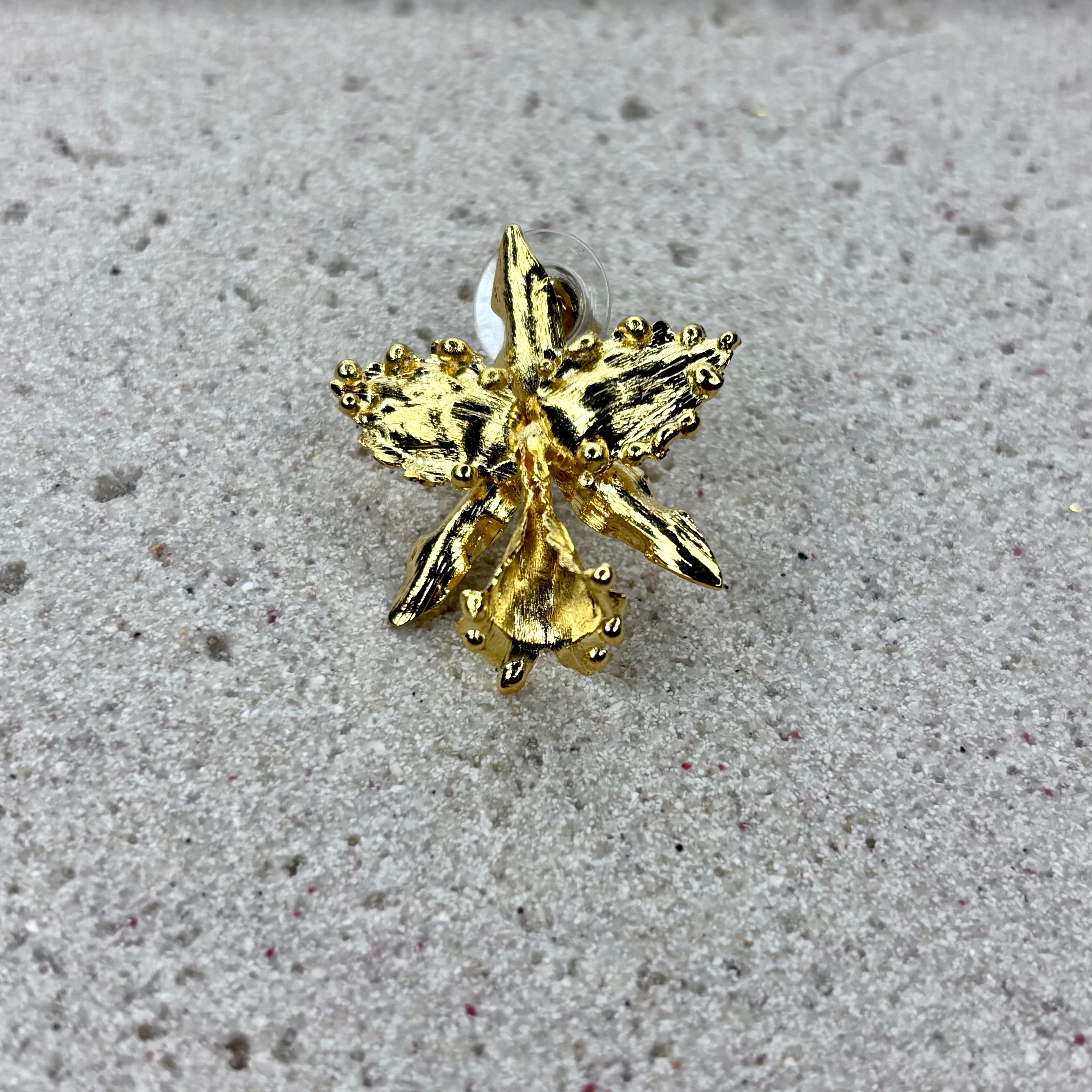 Pair of gold orchid-shaped earrings on a textured surface