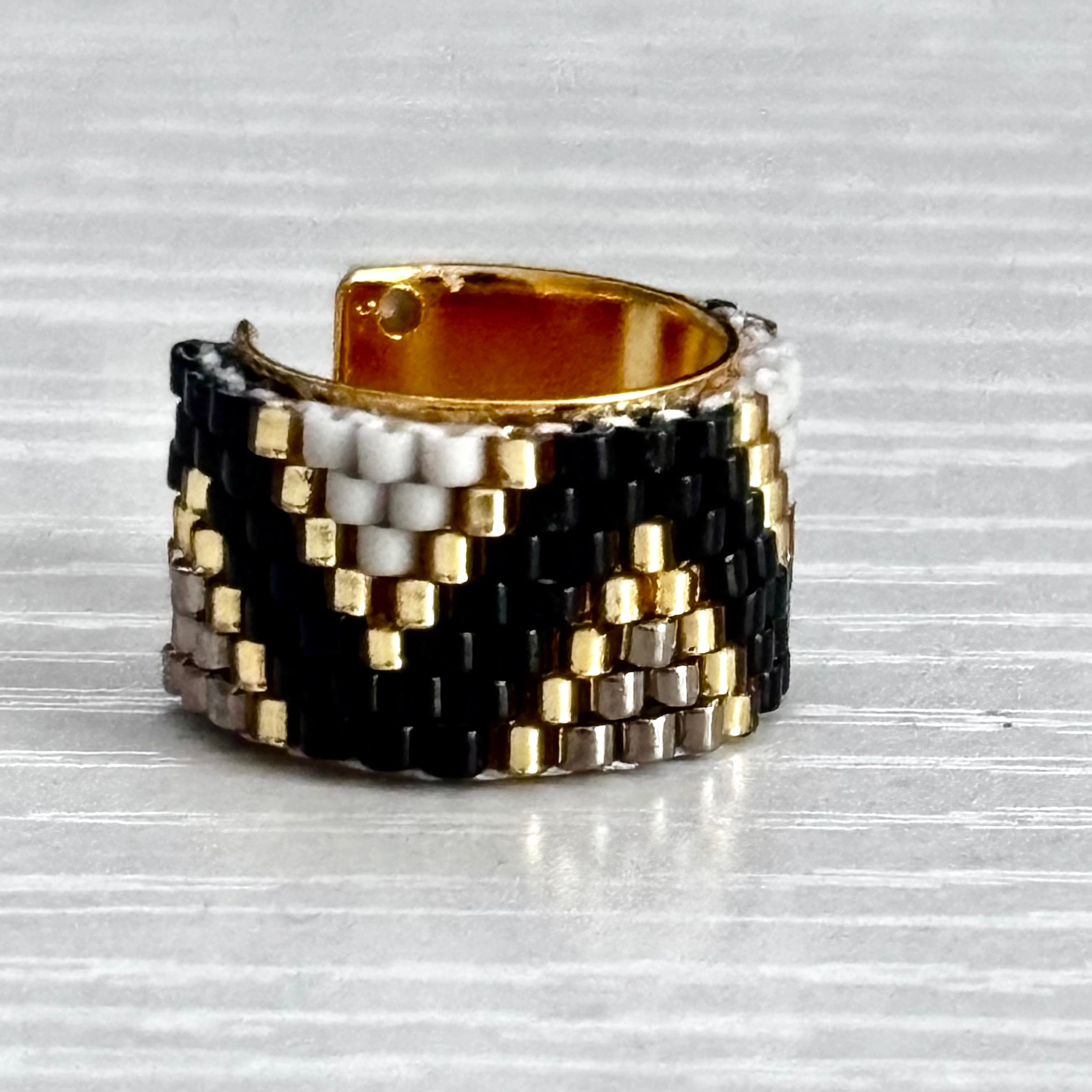 Woven ear cuff with black, gold, and silver pattern on a textured surface