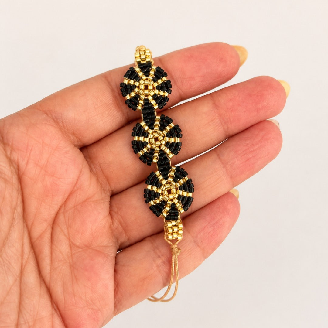 A handmade beaded bracelet with three black and gold floral motifs, held in a person's hand against a plain light background.