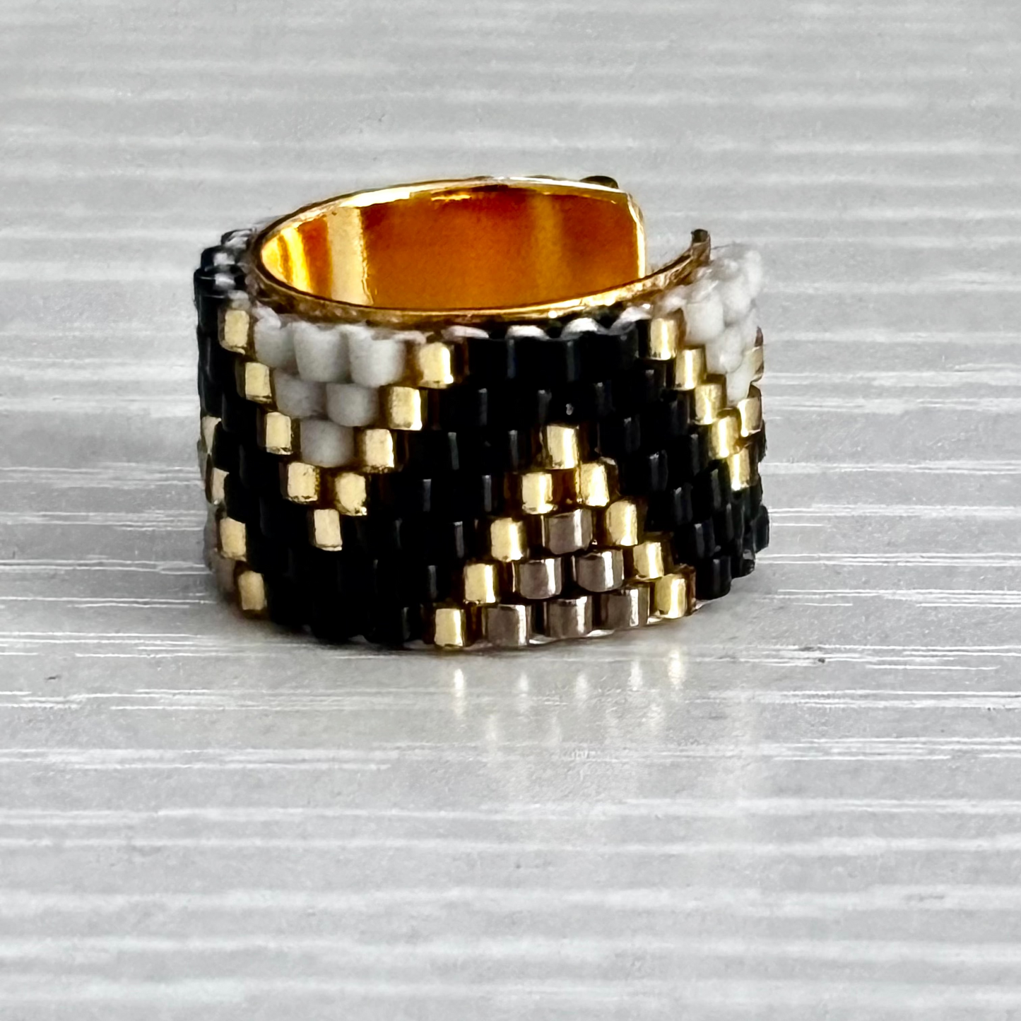 Woven ear cuff with black, gold, and silver pattern on a textured surface