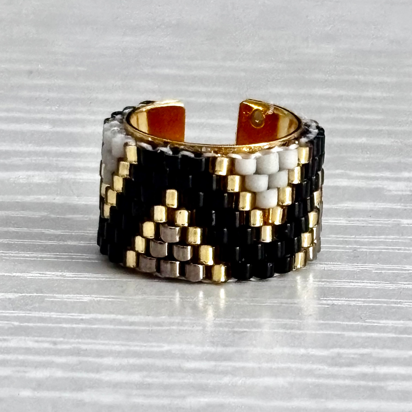 Woven ear cuff with black, gold, and silver pattern on a textured surface