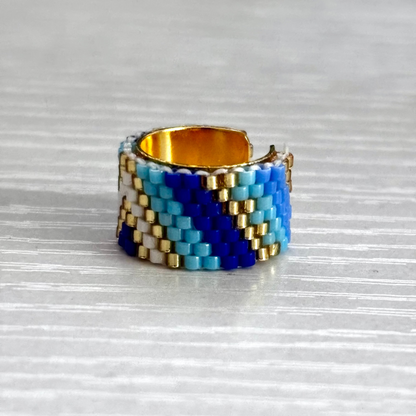 Beaded ear cuff with blue, white, and gold pattern on a reflective surface