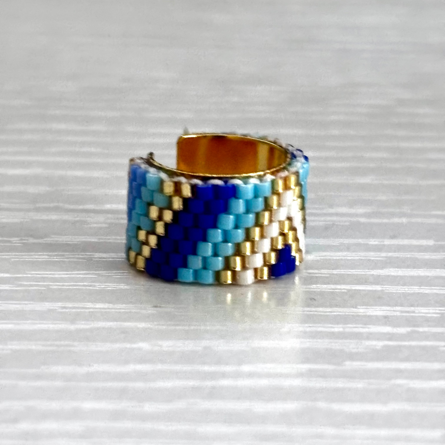 Beaded ear cuff with blue, white, and gold pattern on a reflective surface