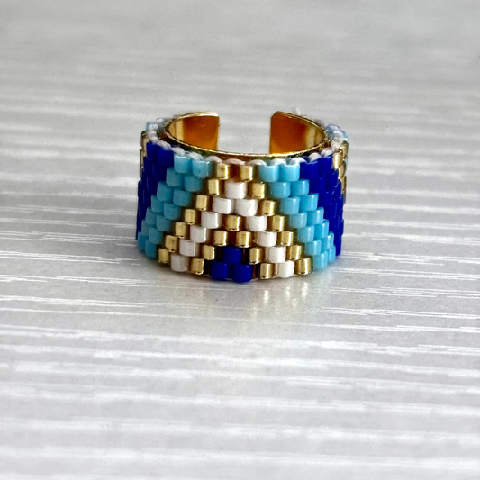 Beaded ear cuff with blue, white, and gold pattern on a reflective surface